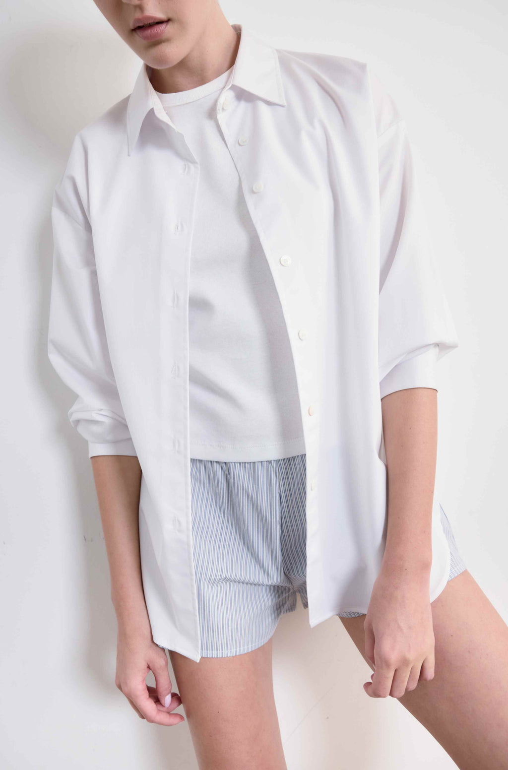 Person wearing a white oversized shirt and striped shorts on a plain background