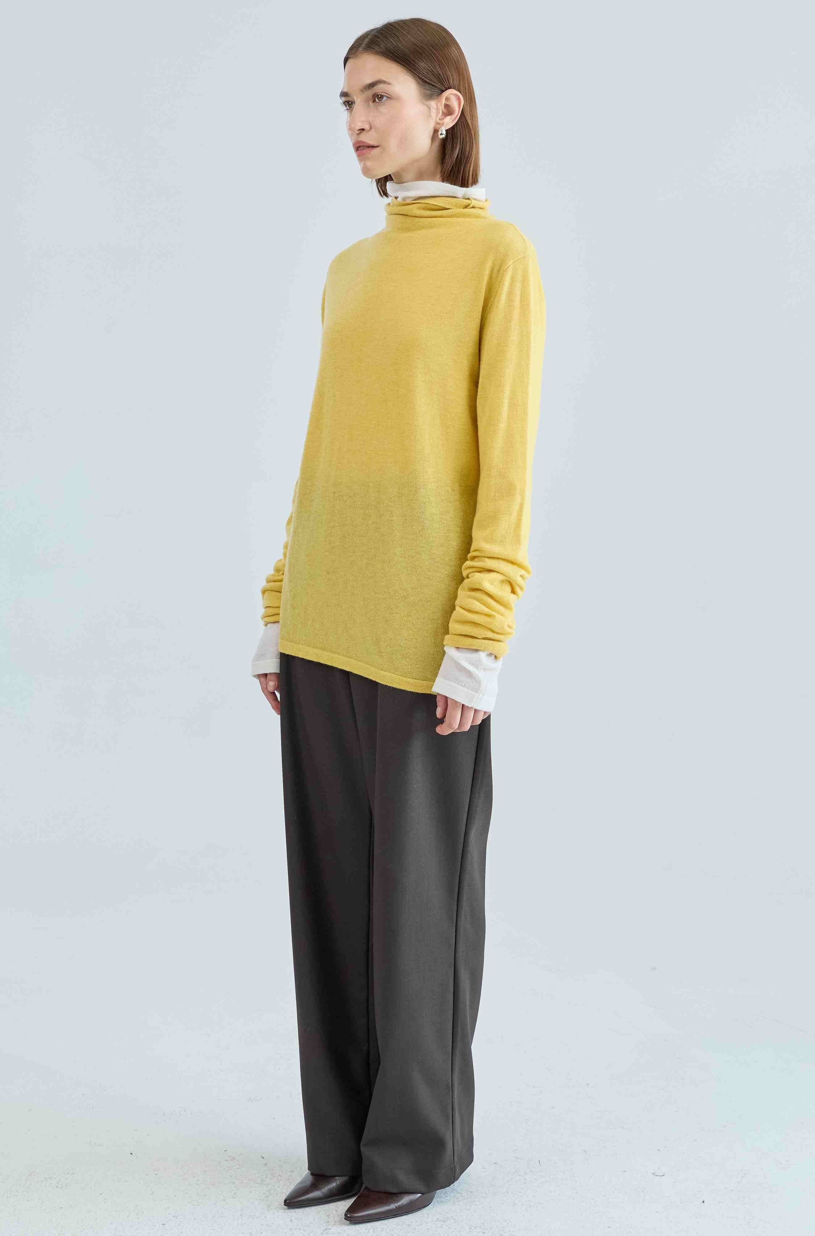 Person wearing a yellow turtleneck and dark pants on a light gray background