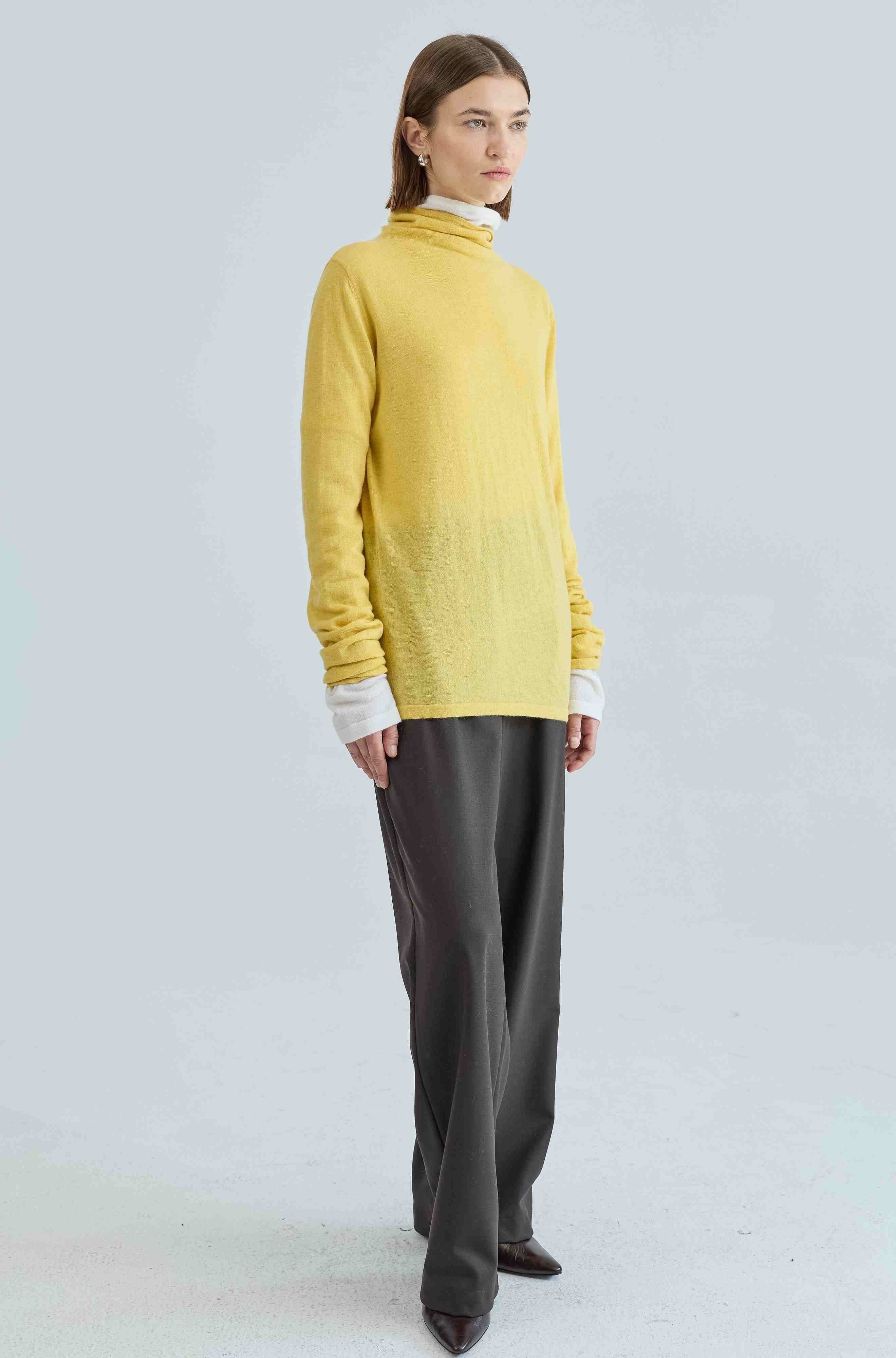 Person wearing a yellow sweater and brown pants on a light gray background