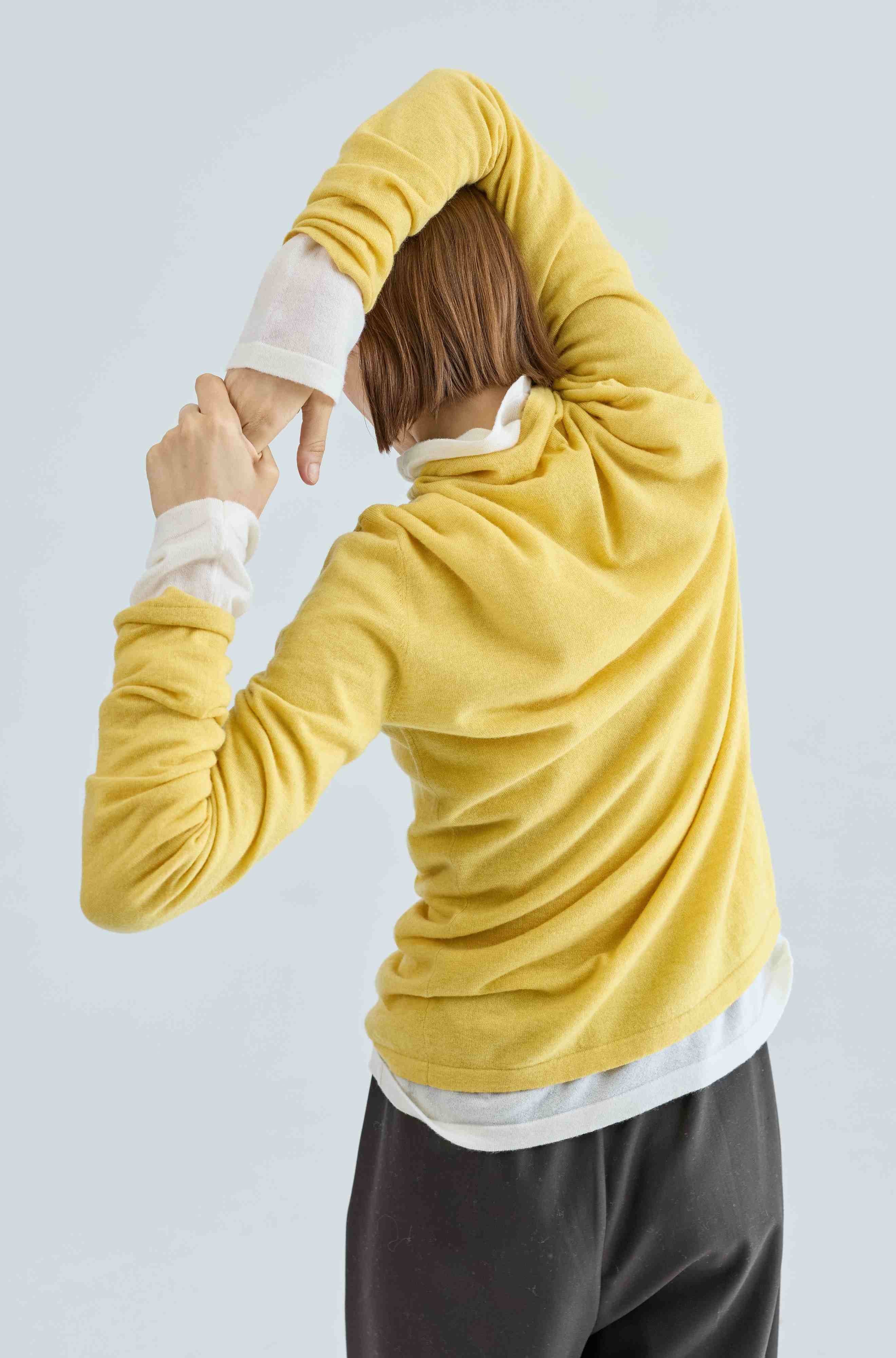 Person wearing a yellow turtleneck over a white turtleneck with a light gray background