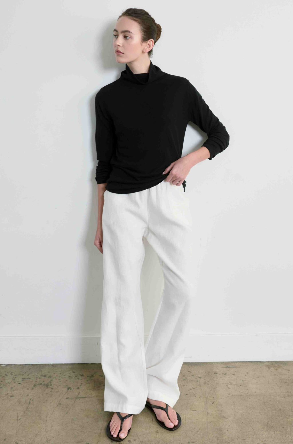 Person wearing a black turtleneck and white pants against a plain background