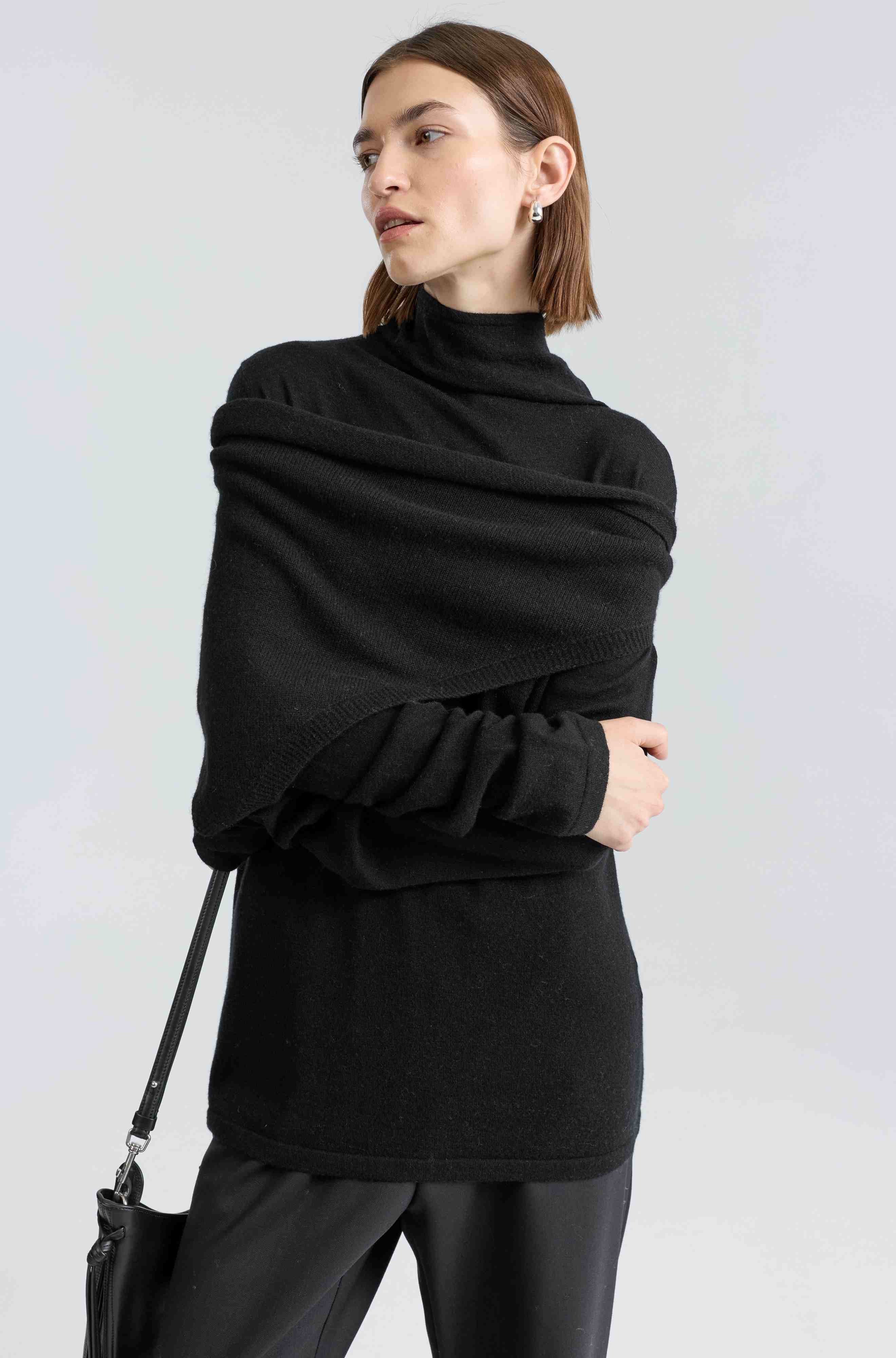 Woman wearing a black turtleneck sweater and black pants against a white background