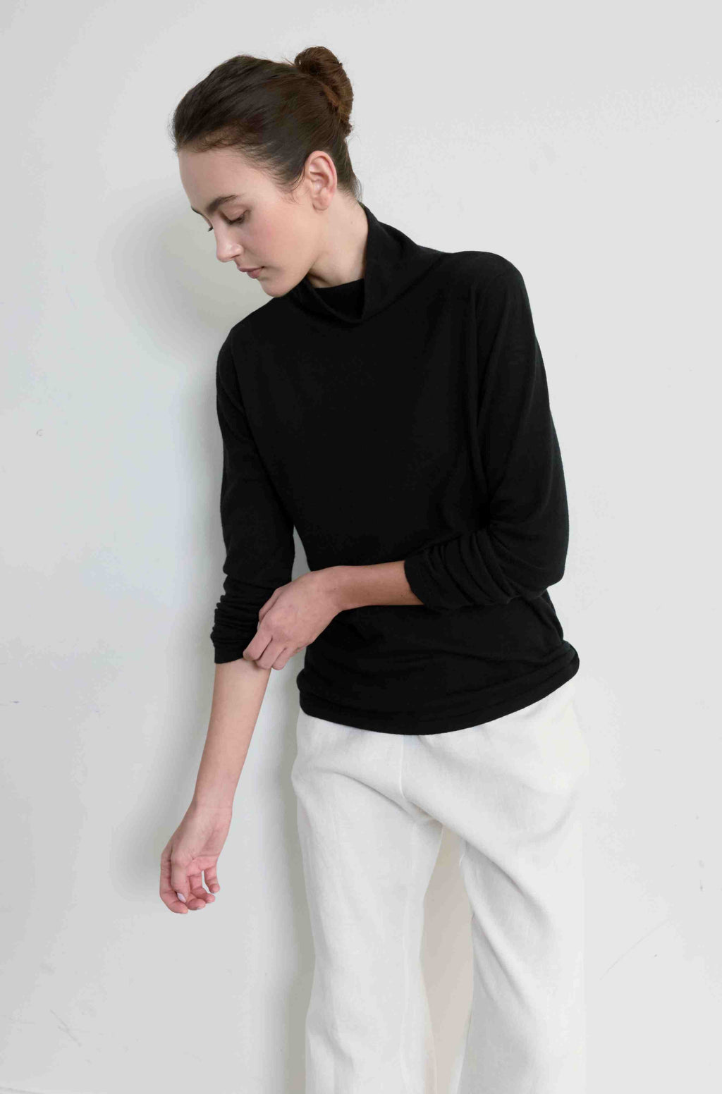 Woman wearing a black turtleneck and white pants against a light background