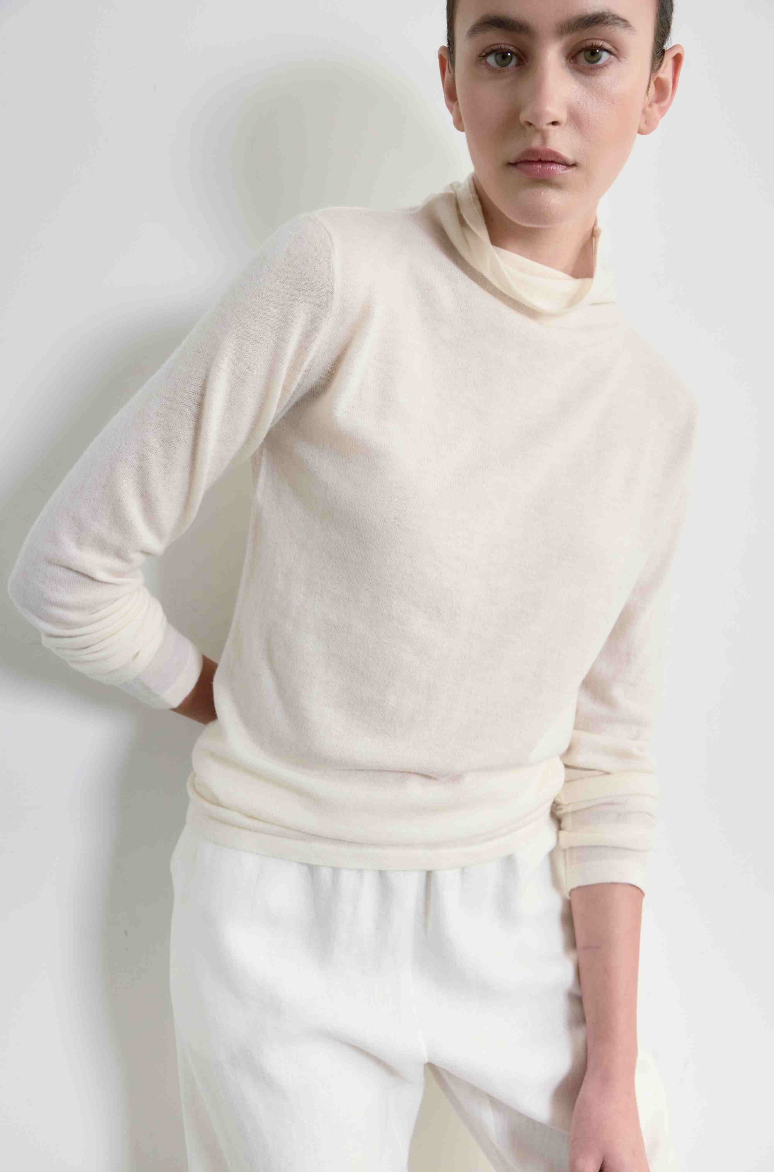 Person wearing a cream-colored sweater and pants against a white background