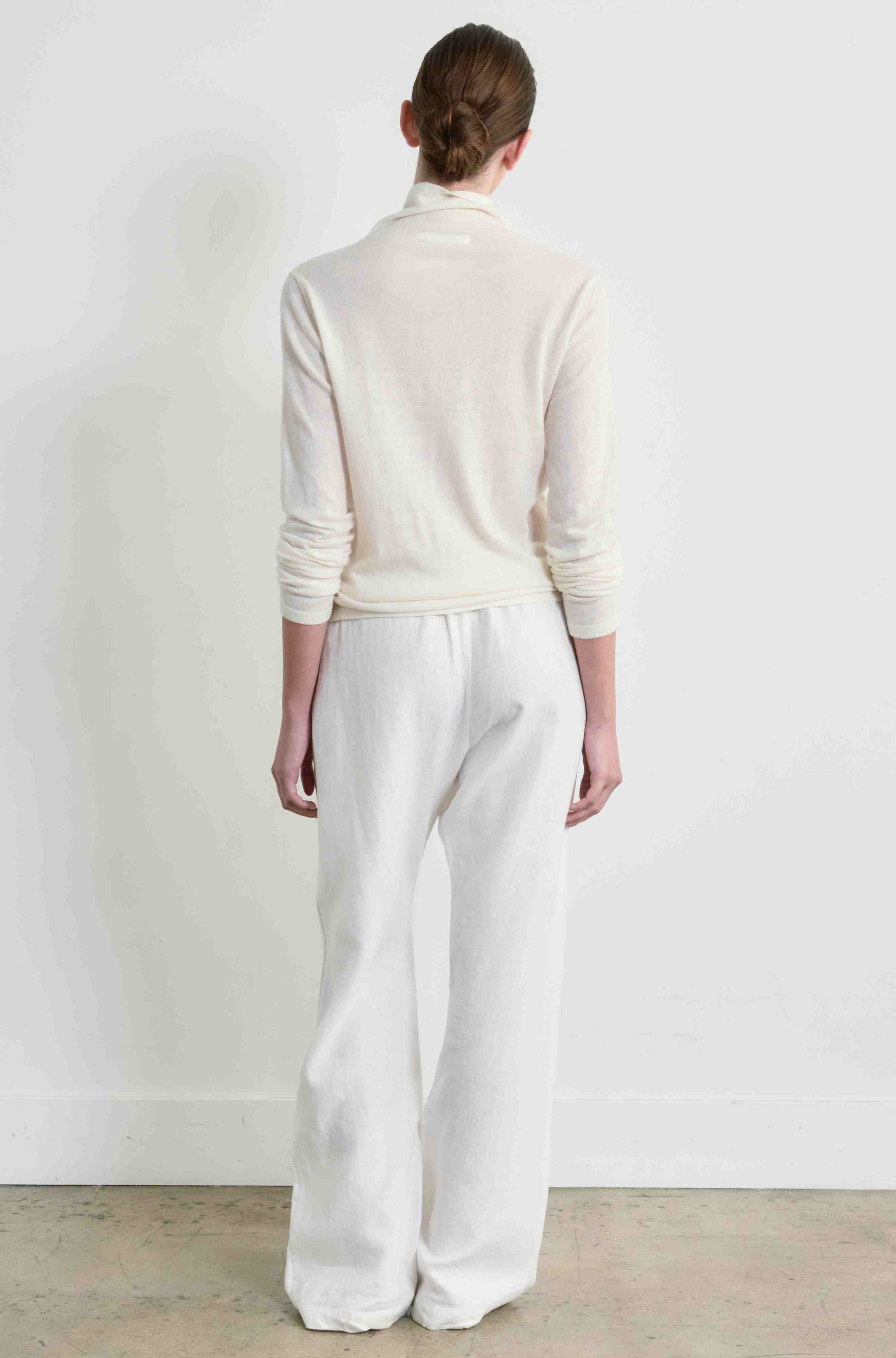 Person wearing a light-colored shirt and white pants against a plain background