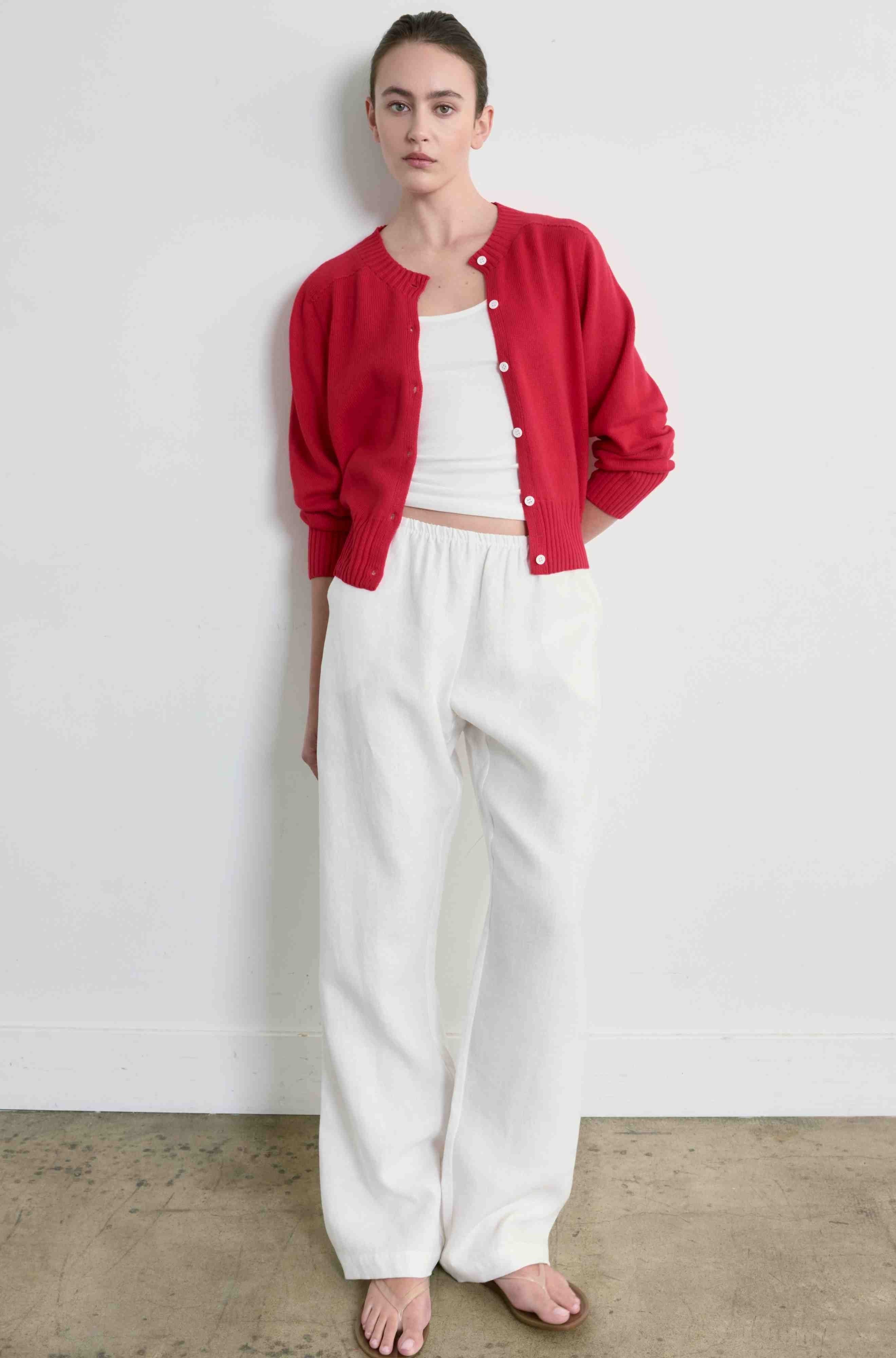 Woman wearing a red button up cardigan with  white tank and white pants