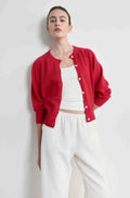 Person wearing a red cardigan over a white top and pants on a light gray background