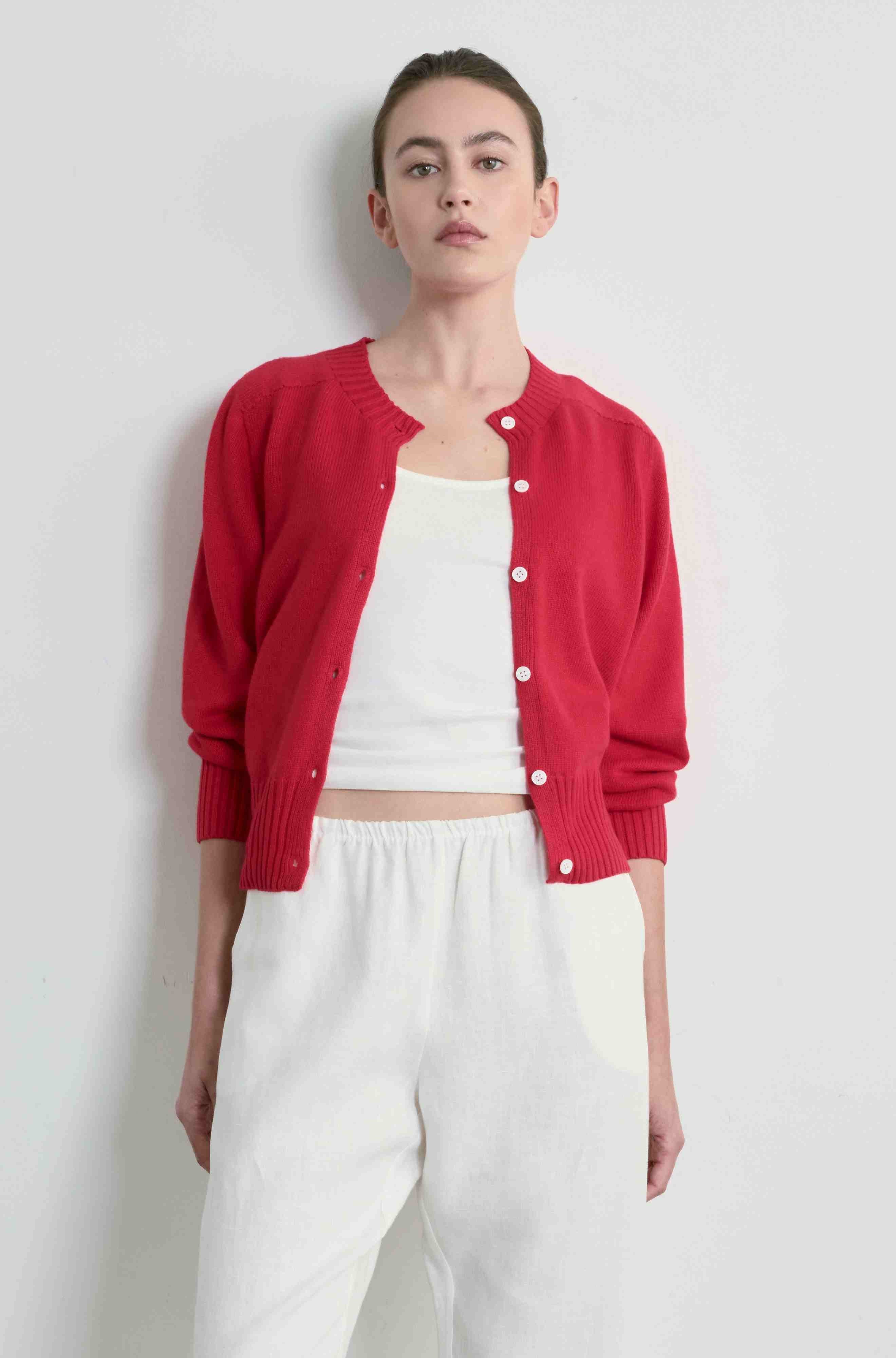 Person wearing a red cardigan over a white top and pants on a light gray background