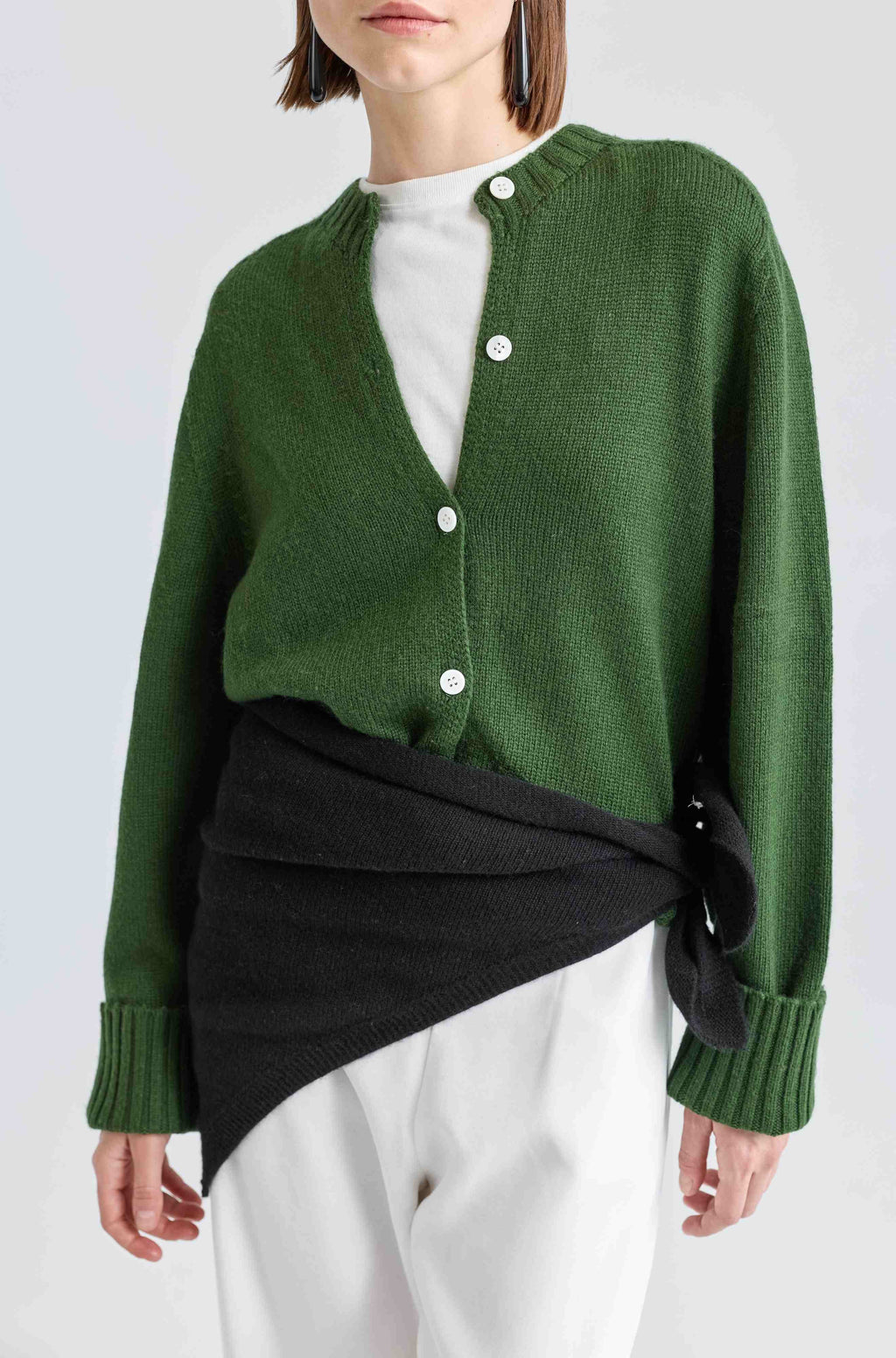 Person wearing a green cardigan over a black and white outfit on a light gray background