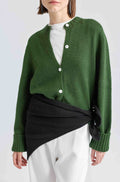 Person wearing a green cardigan over a black and white outfit on a light gray background