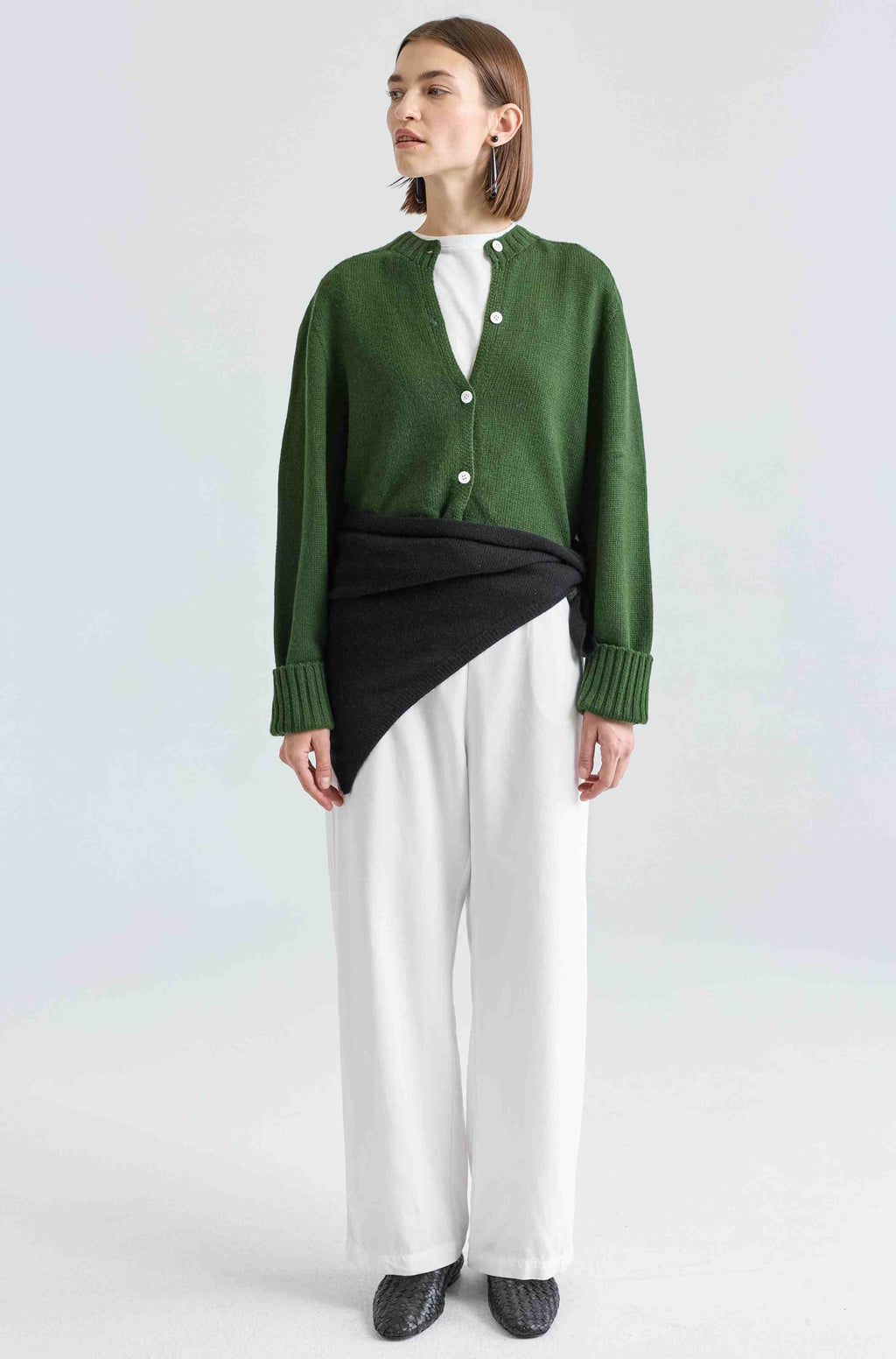Person wearing a green cardigan over a white shirt with a black and white skirt on a white background