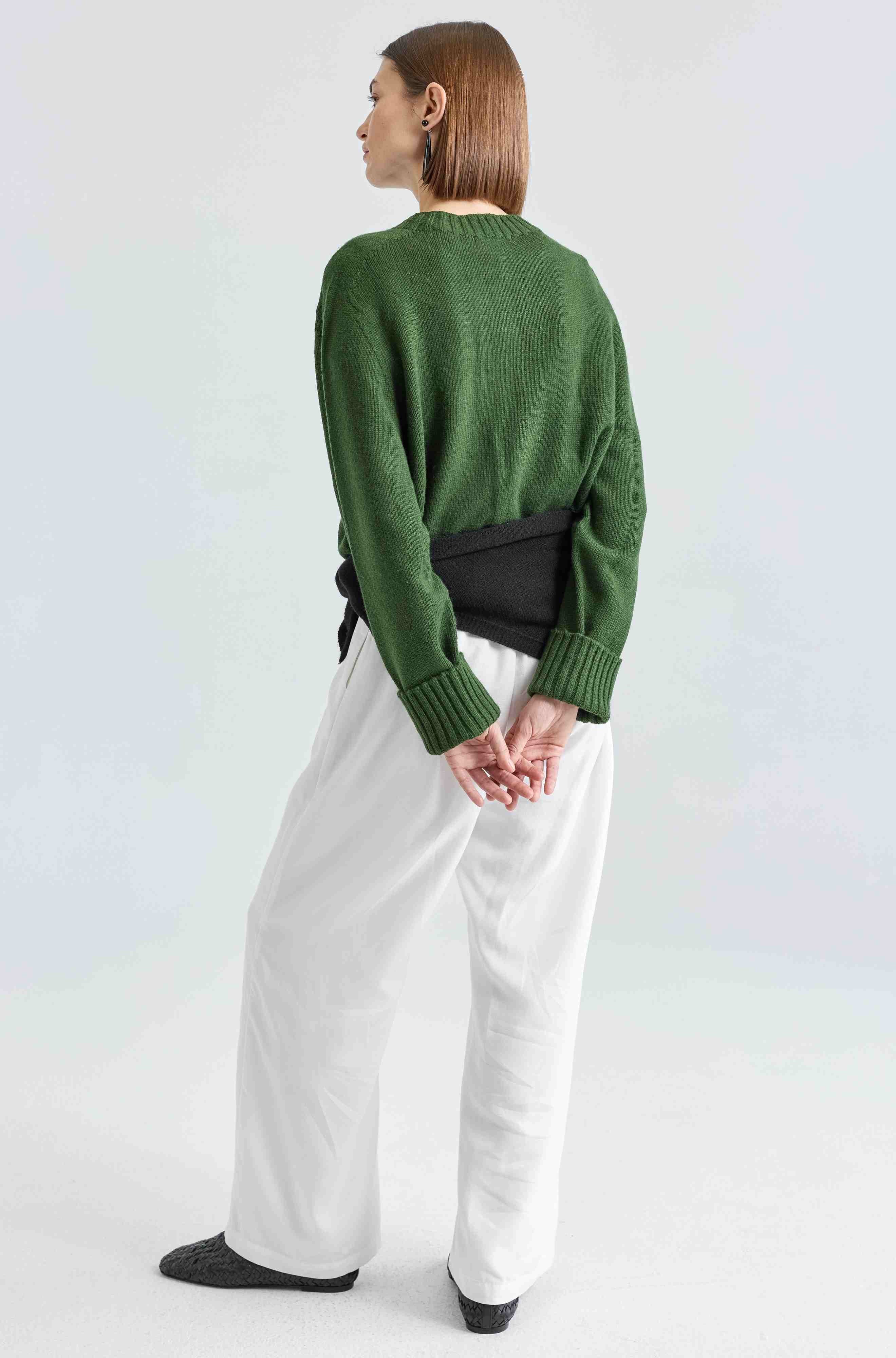 Person wearing a green sweater and white pants on a light gray background