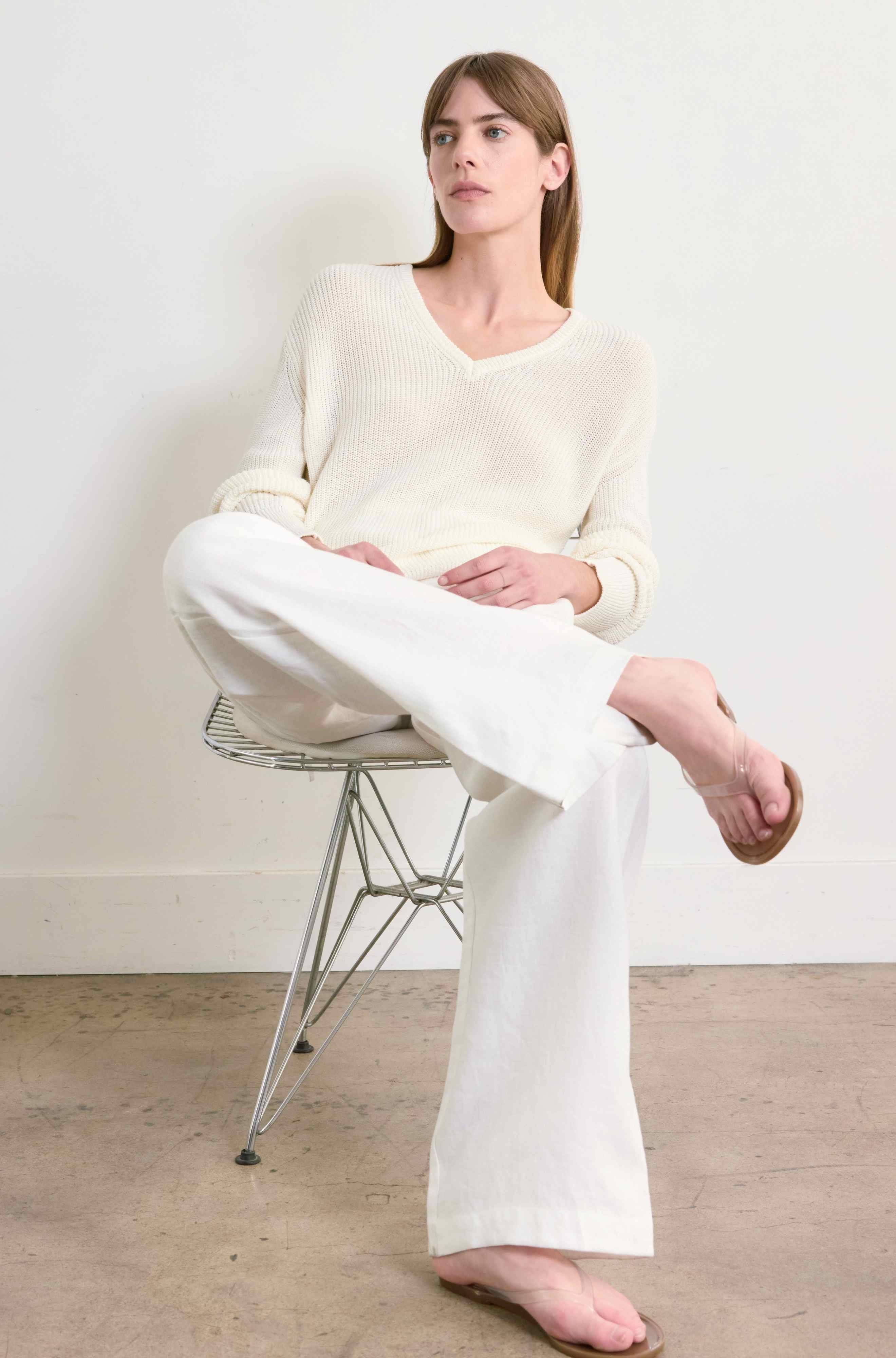 Person wearing a white outfit sitting on a chair against a plain background