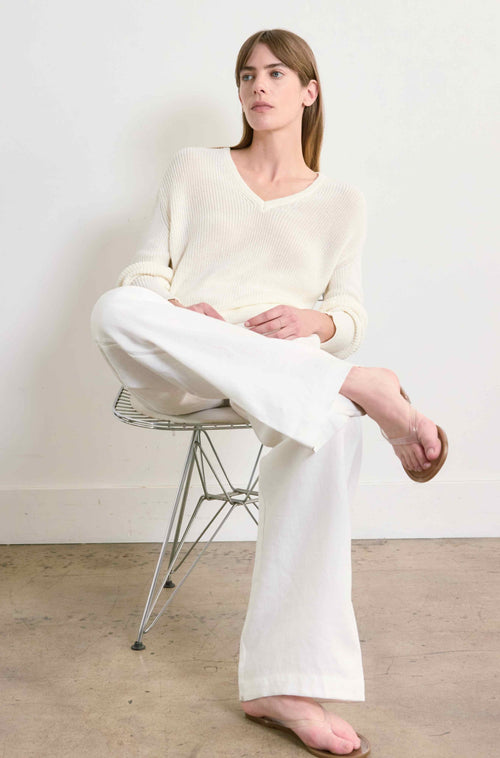 Person wearing a white outfit sitting on a chair against a plain background