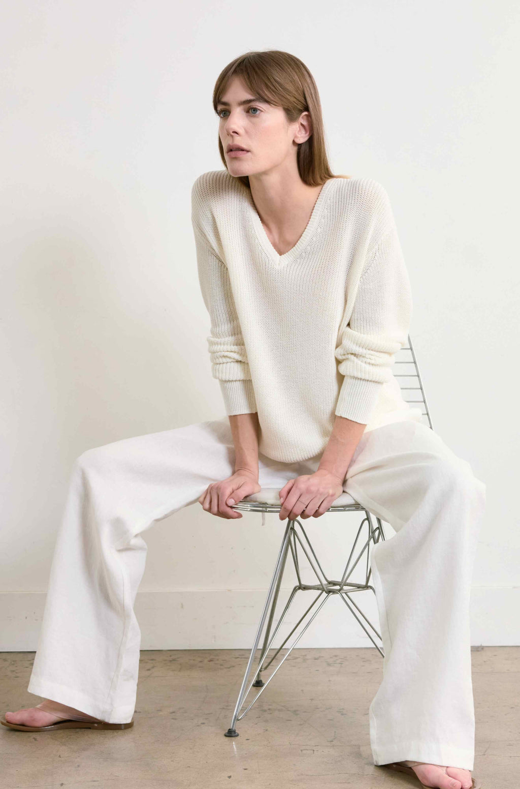 Woman wearing a white outfit sitting on a chair against a plain background