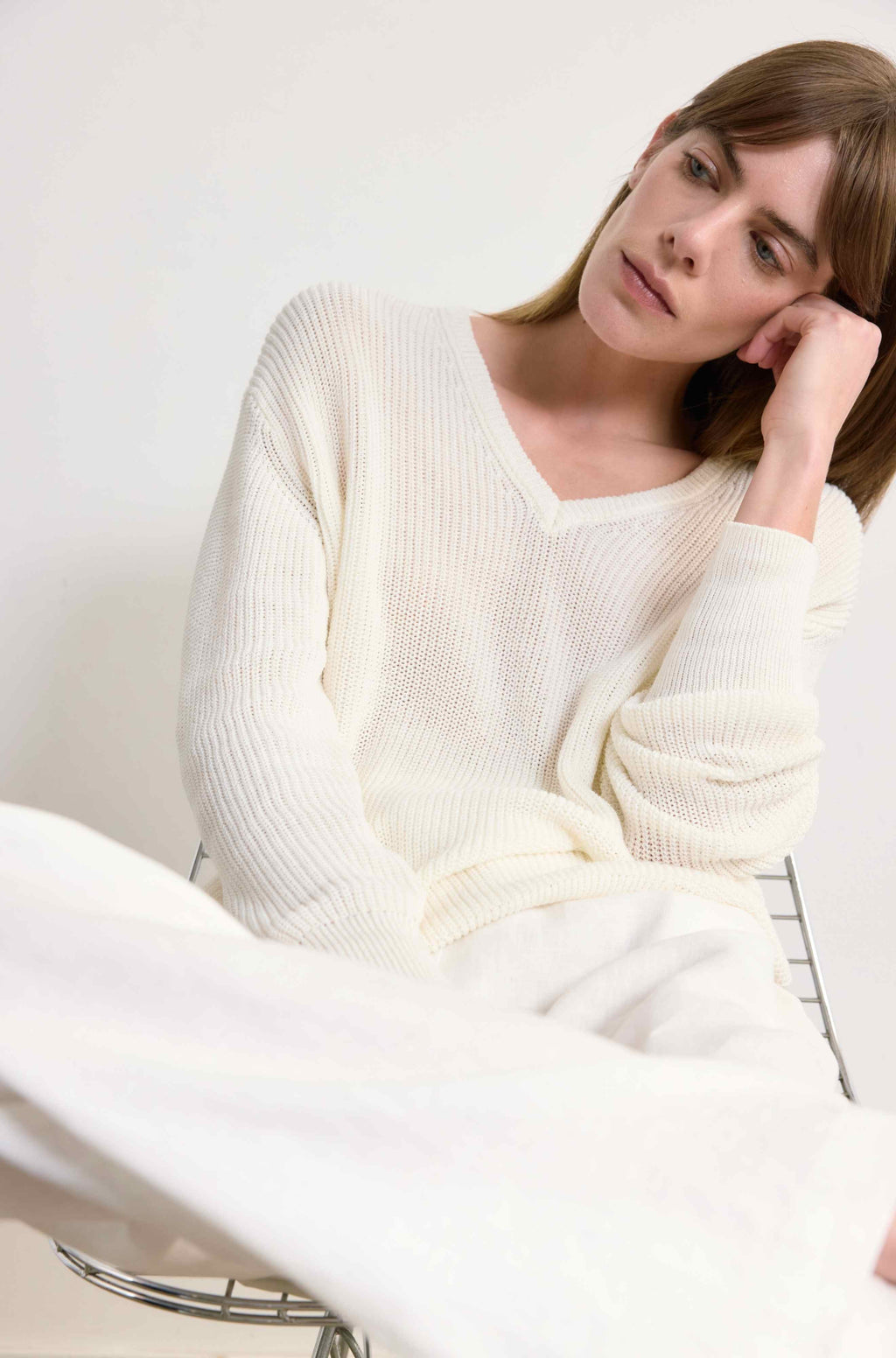 Woman wearing a white sweater sitting on a white couch.