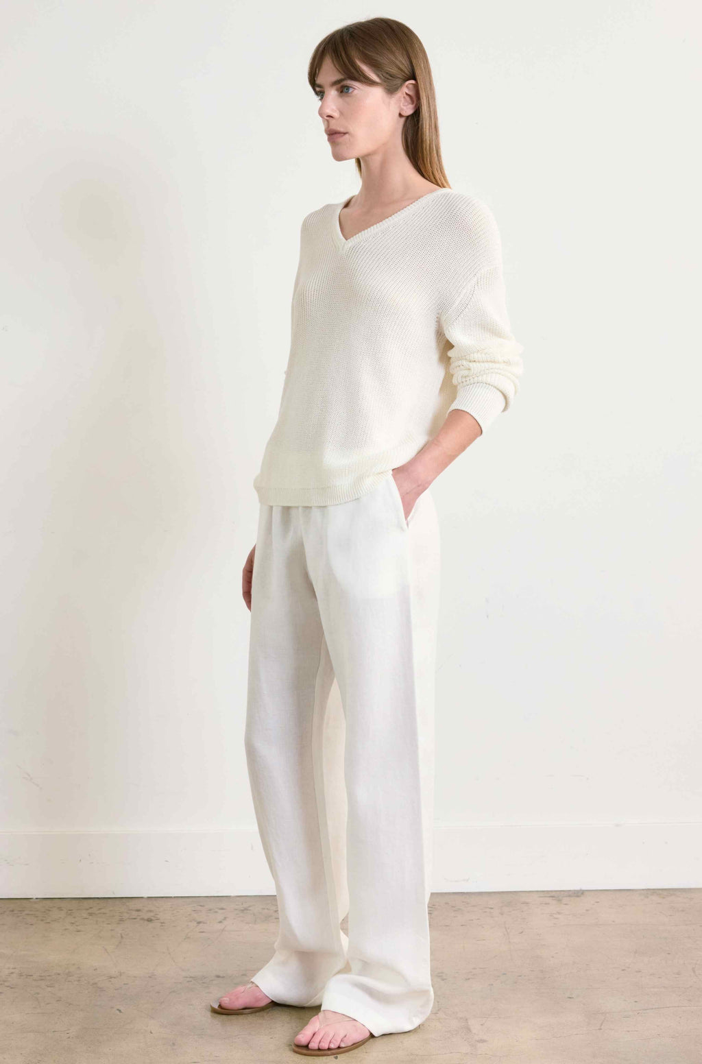 Woman wearing a white sweater and pants against a plain background