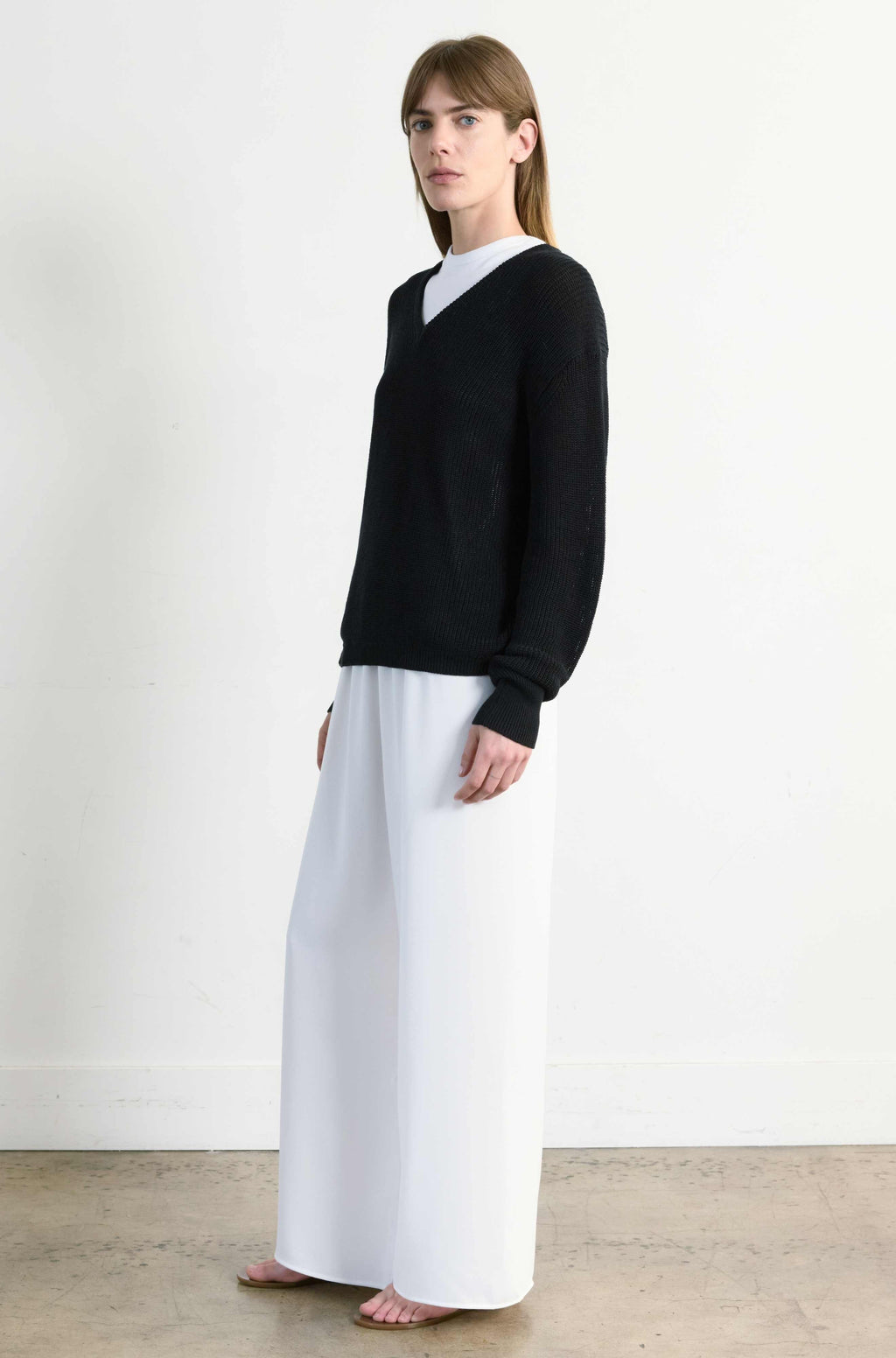 Person wearing a black sweater and white pants on a plain background