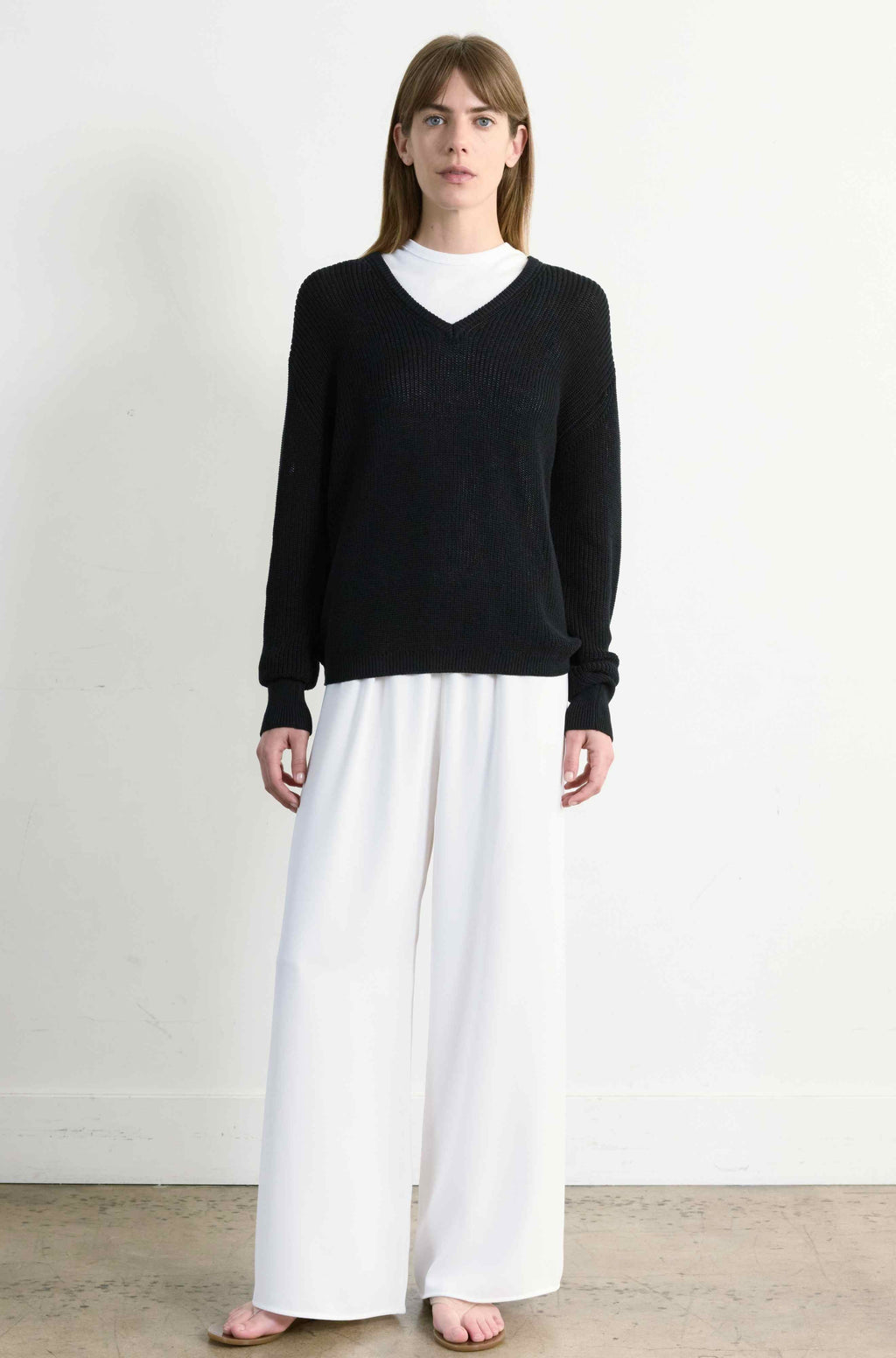 Person wearing a black sweater and white skirt against a plain background