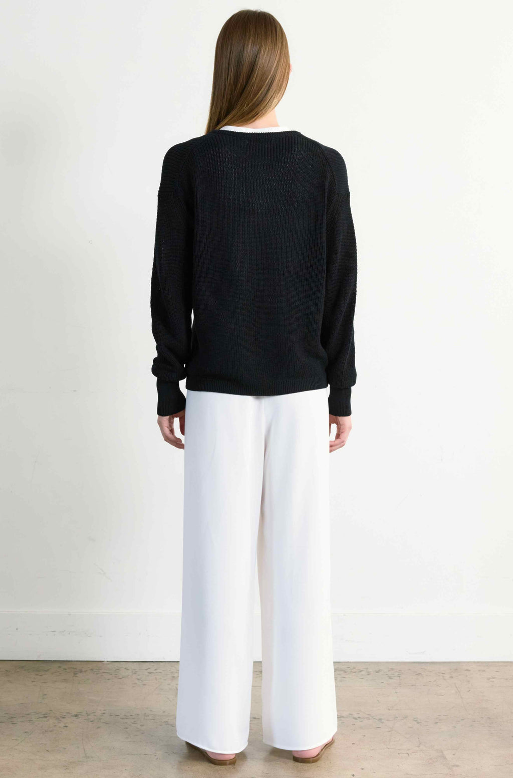 Person wearing a black sweater and white pants against a plain background