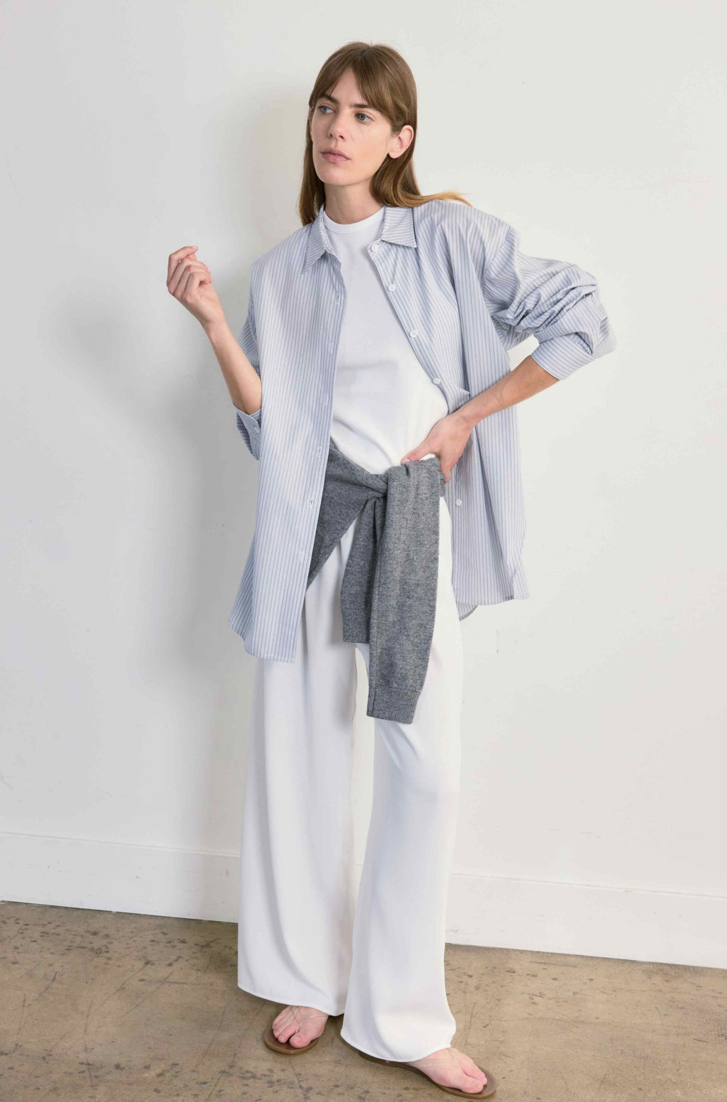 Woman wearing a light blue shirt, white pants, and gray scarf against a plain background