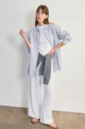 Woman wearing a light blue shirt, white pants, and gray scarf against a plain background