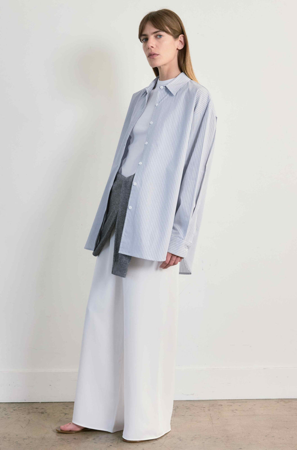 Woman wearing a light blue shirt and white pants against a plain background