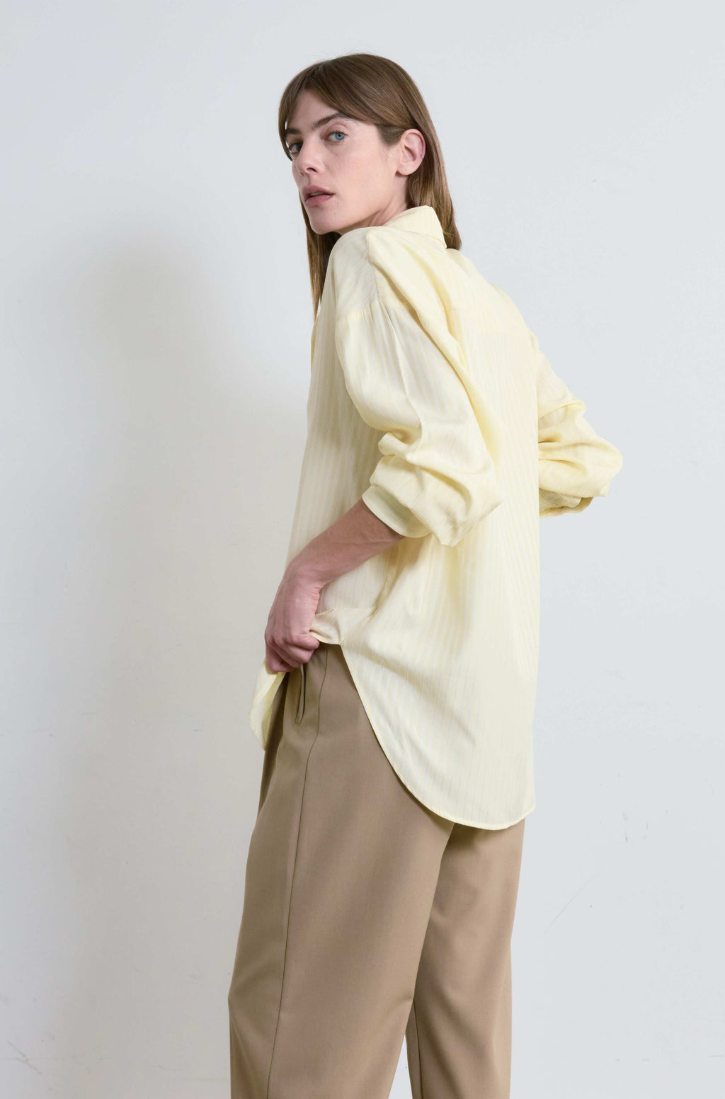 Woman wearing a light yellow blouse and beige pants against a white background