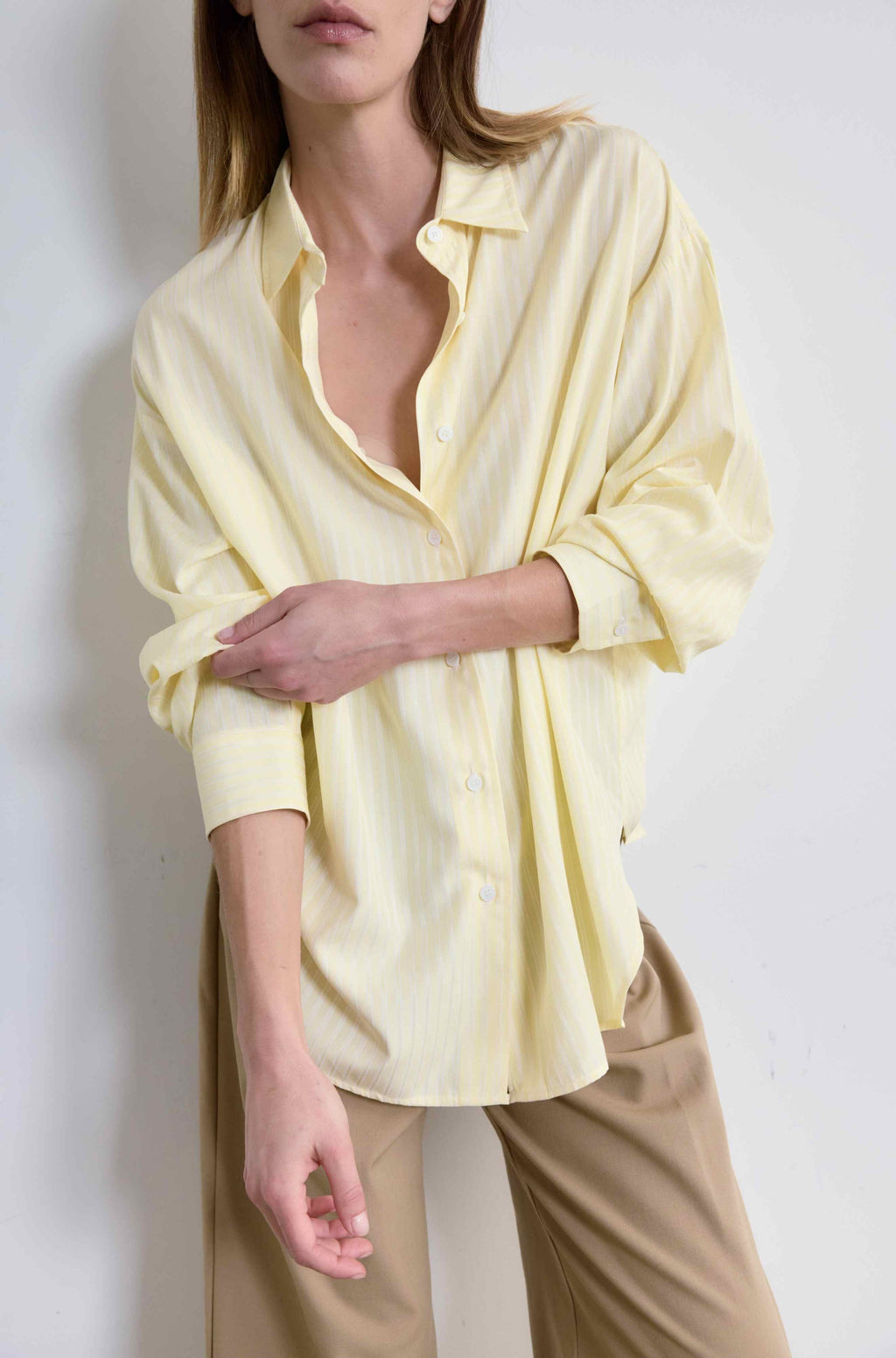 Person wearing a light yellow shirt with rolled-up sleeves on a white background