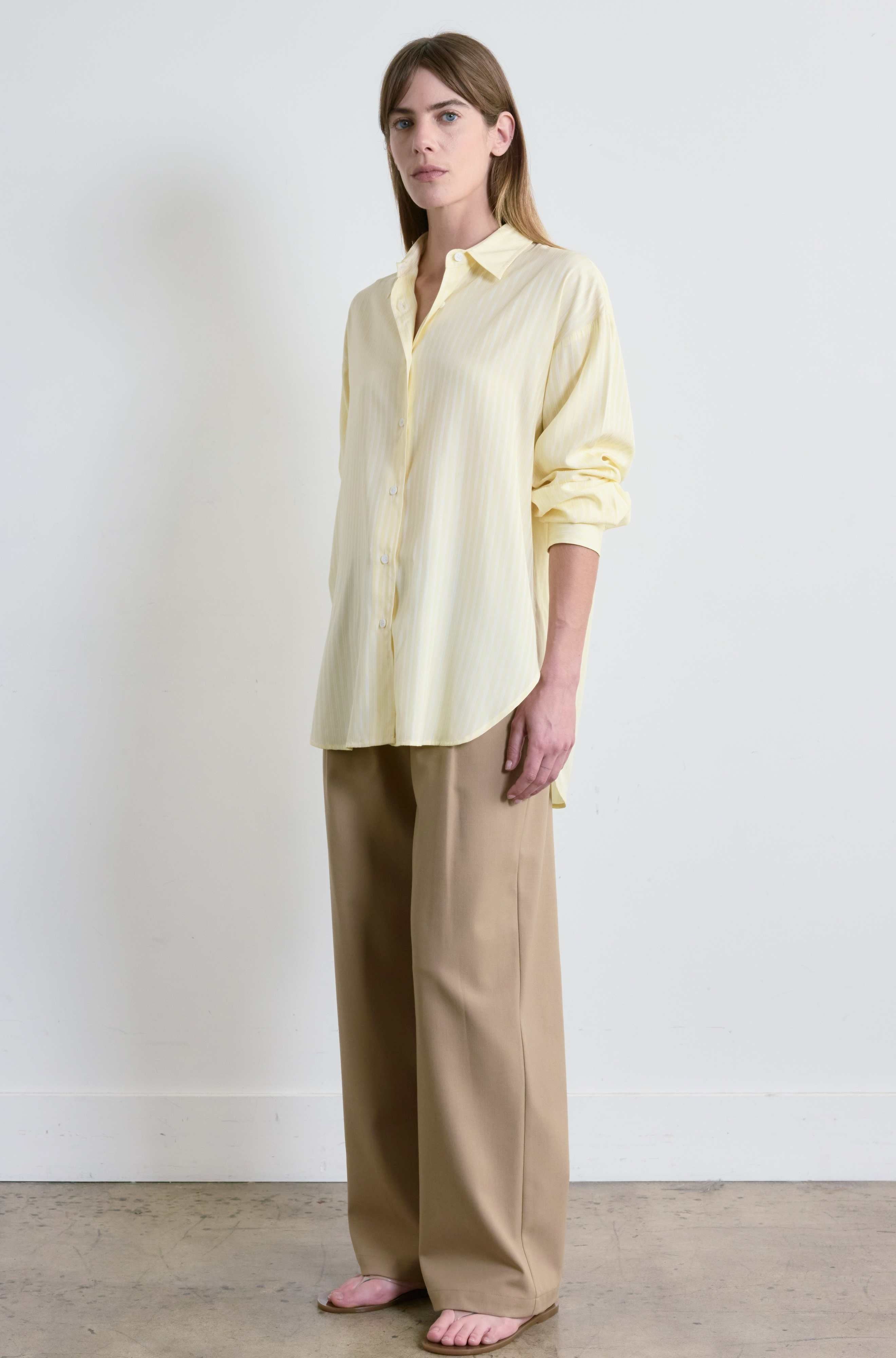 Woman wearing a light yellow blouse and beige pants against a white background