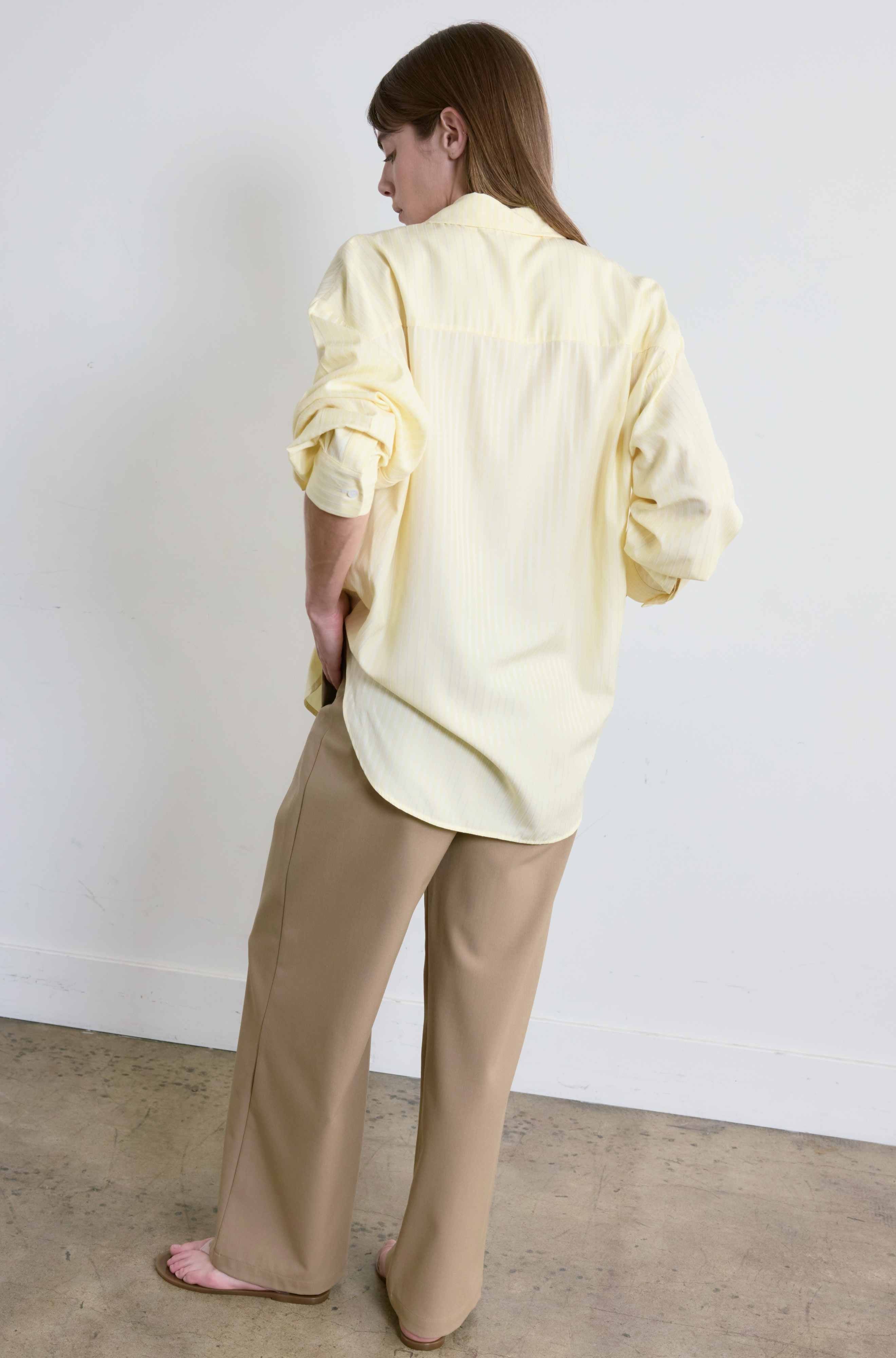 Person wearing a light yellow shirt and beige pants against a white wall.
