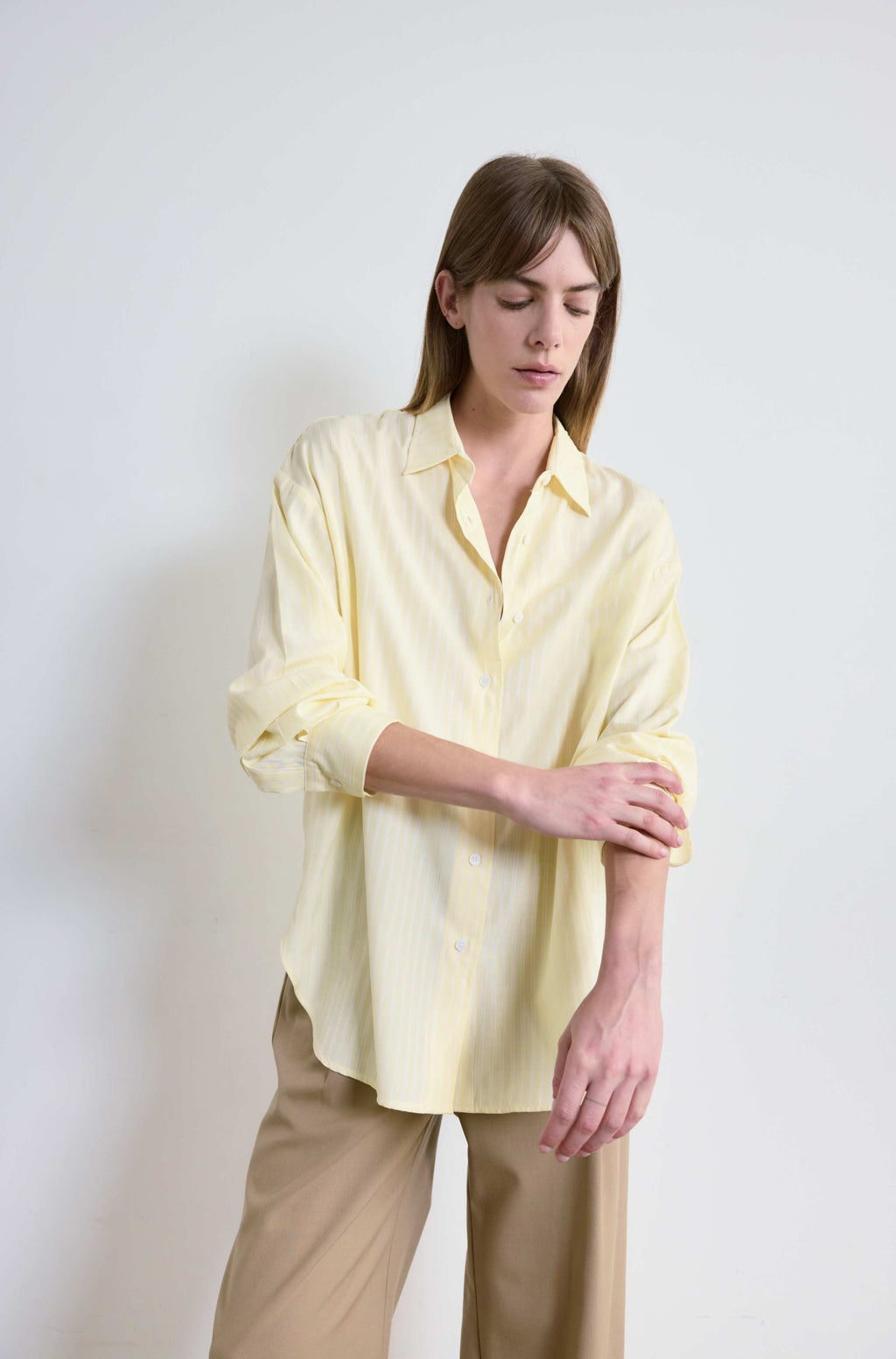 Woman wearing a light yellow shirt and beige pants against a white background