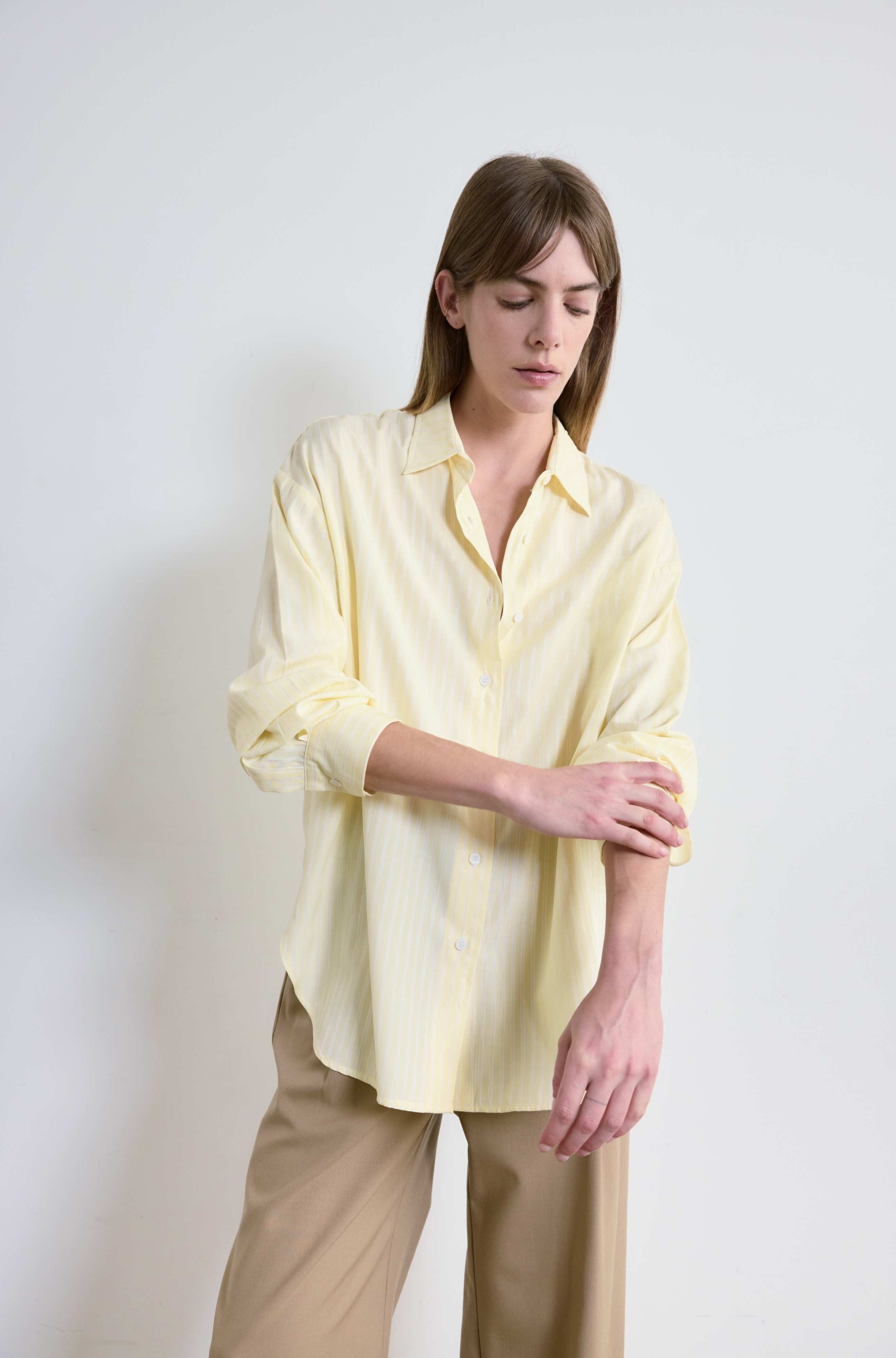 Woman wearing a light yellow shirt and beige pants against a white background