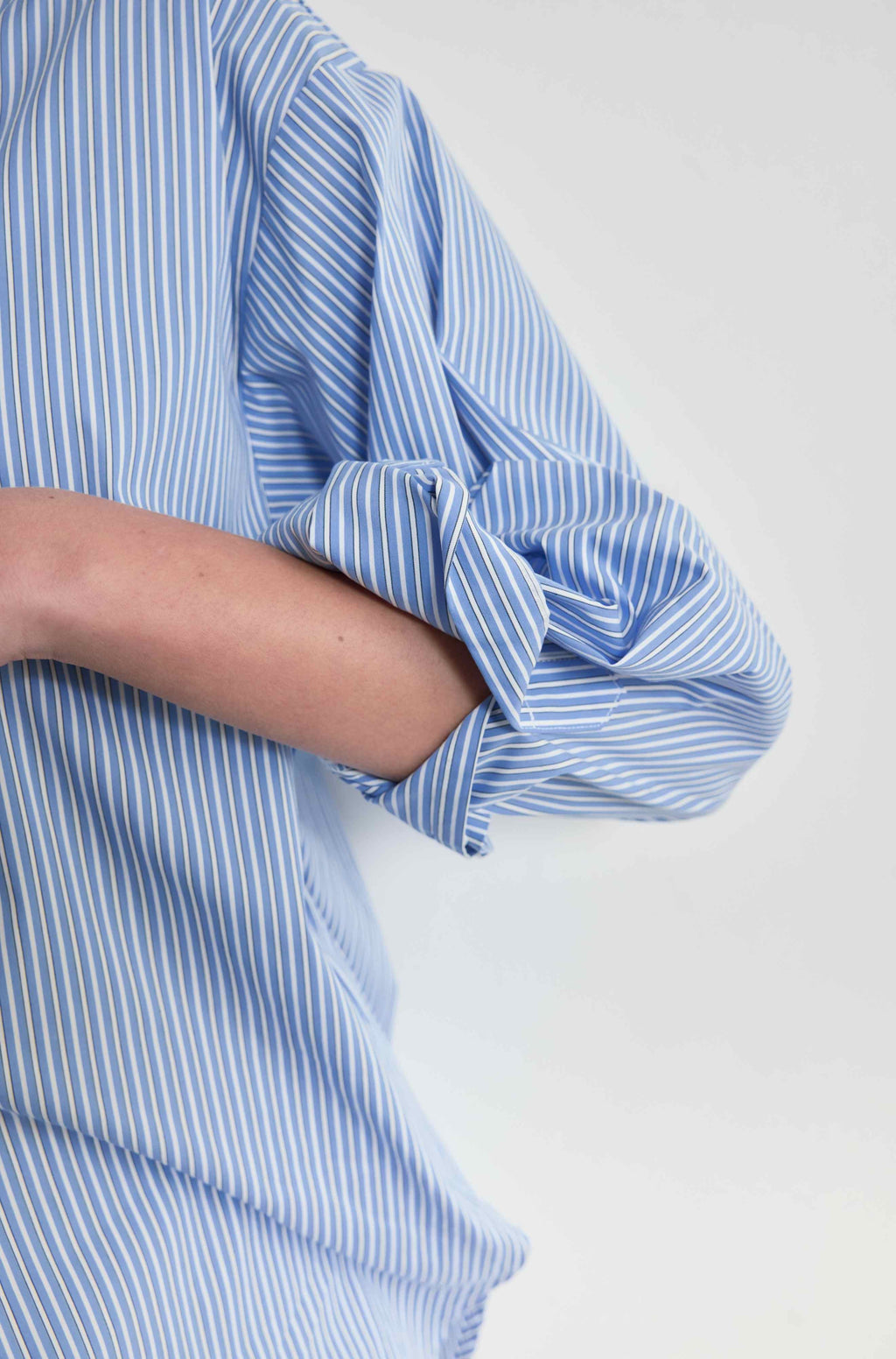 Close-up of a person wearing a blue and white striped shirt with rolled-up sleeves on a light gray background.