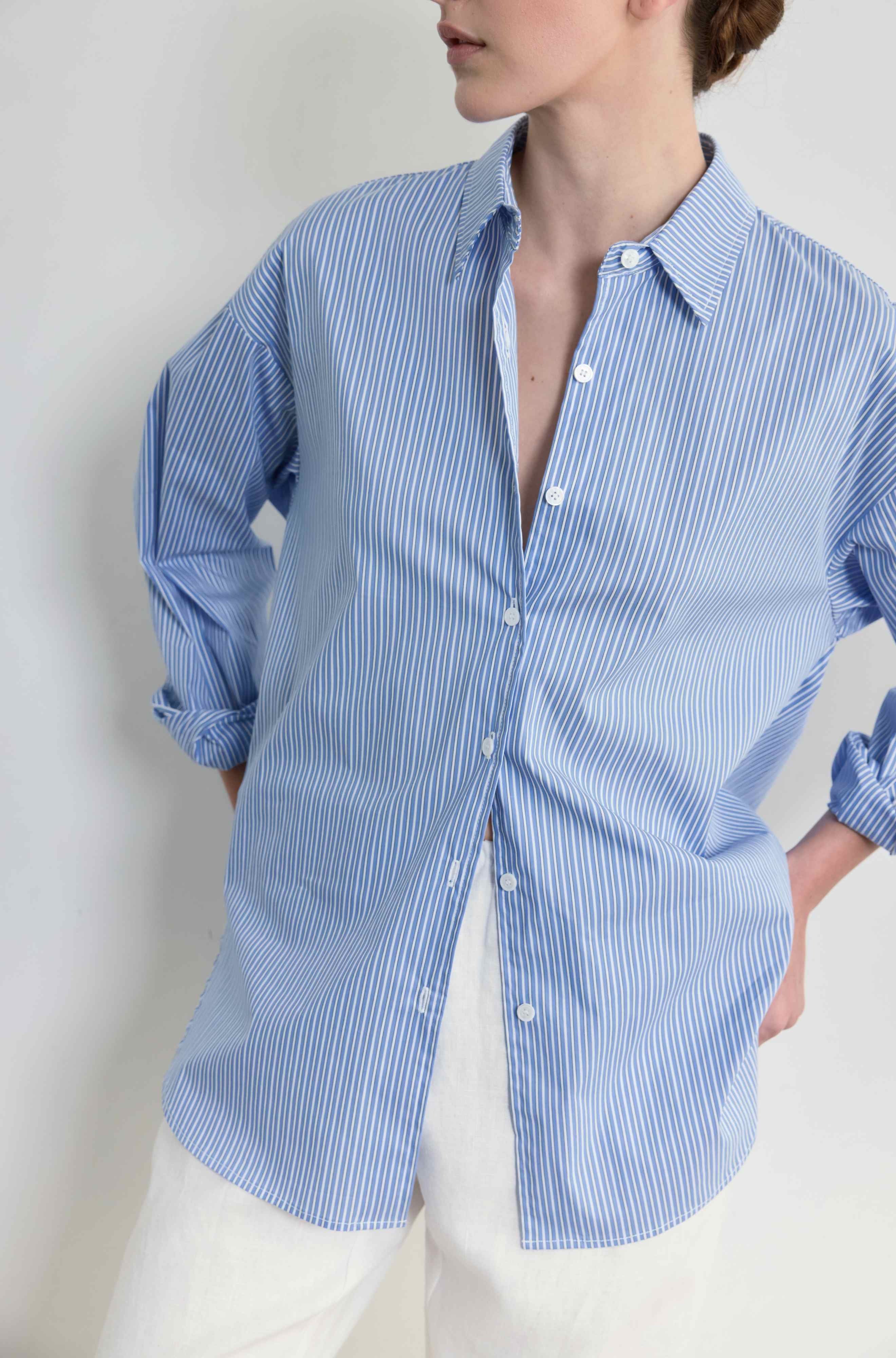 Person wearing a blue striped shirt with rolled-up sleeves against a plain background