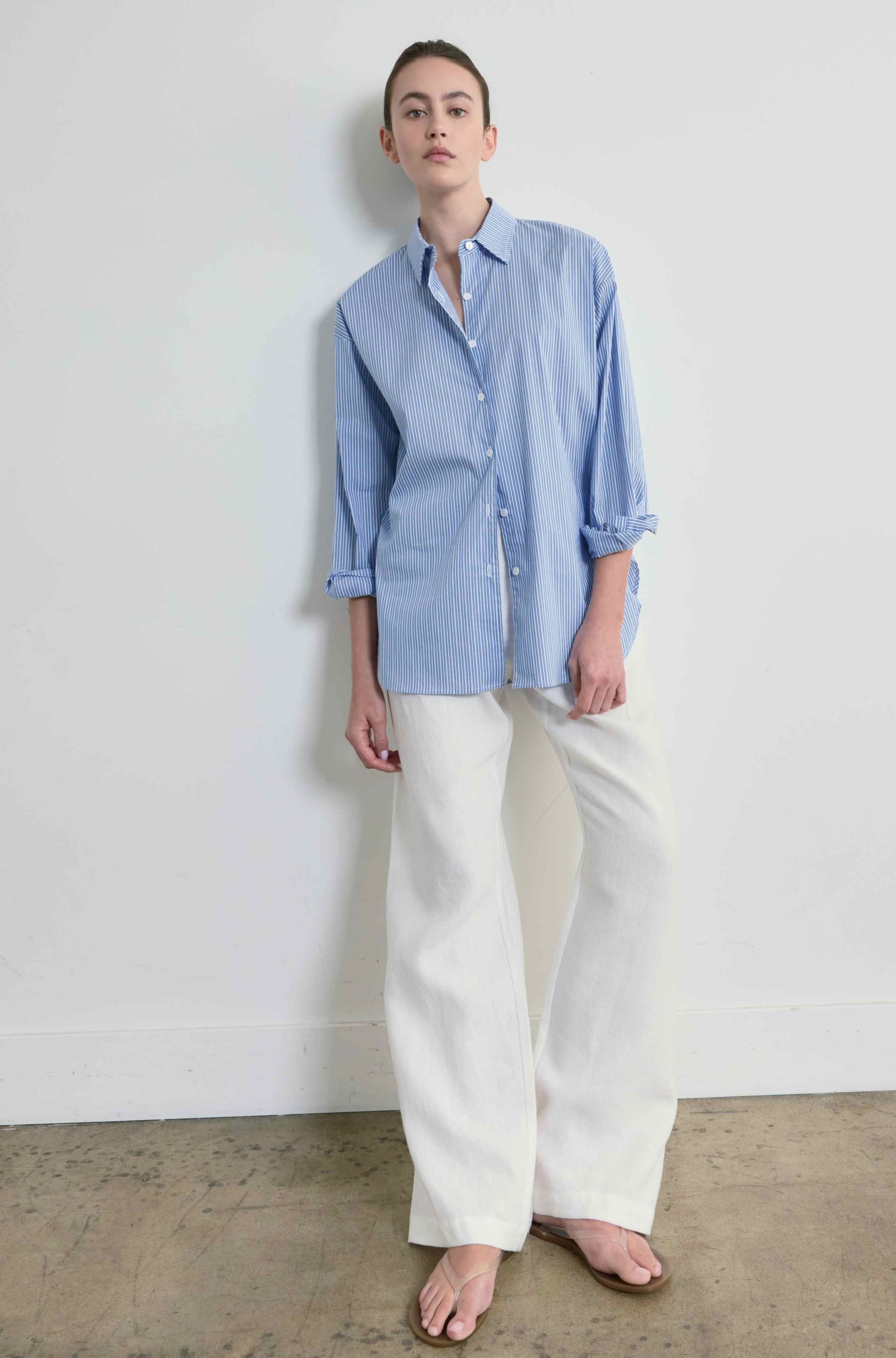 Person wearing a blue striped shirt and white pants against a plain background