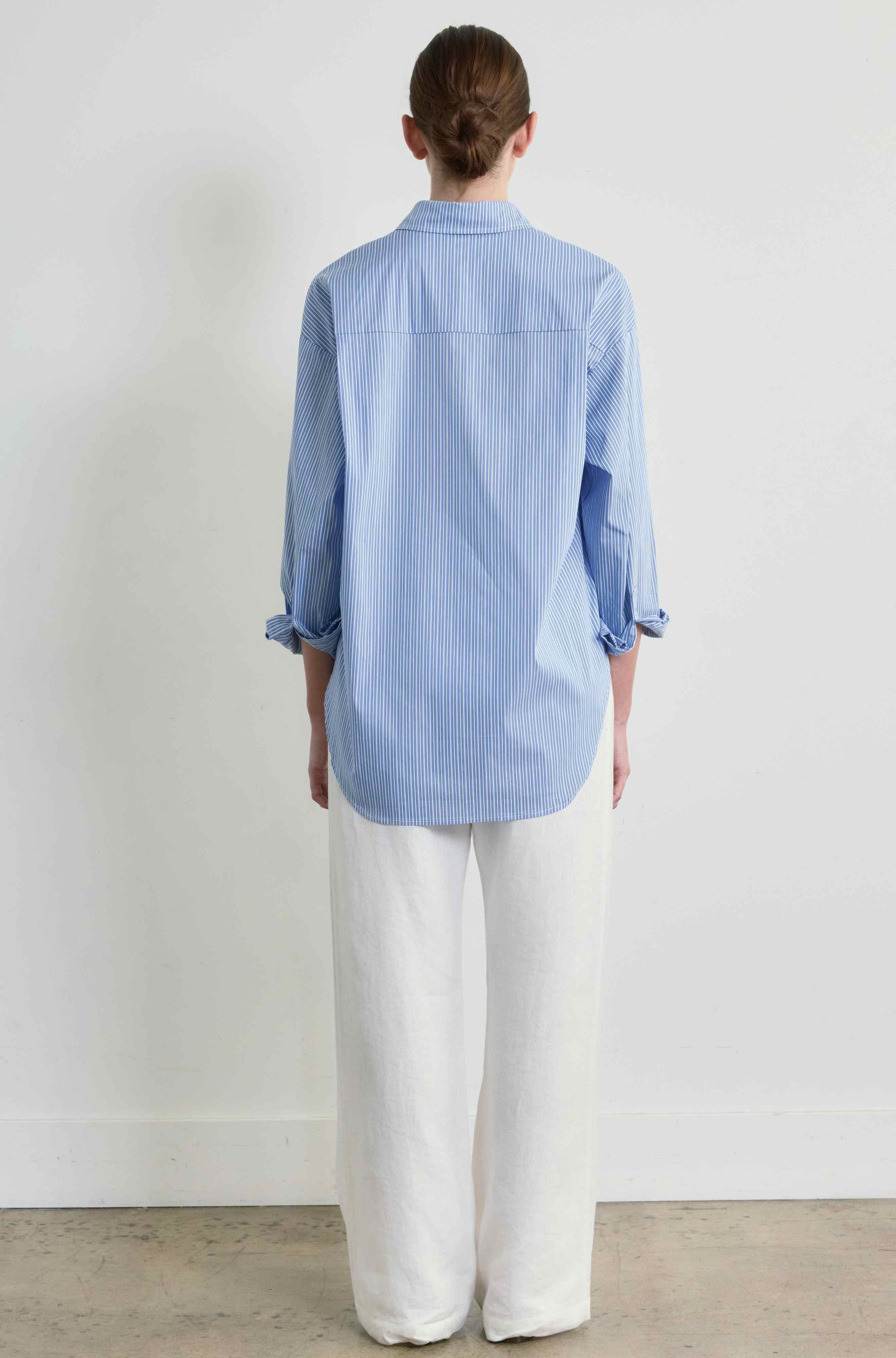 Person wearing a blue striped shirt and white pants against a plain background