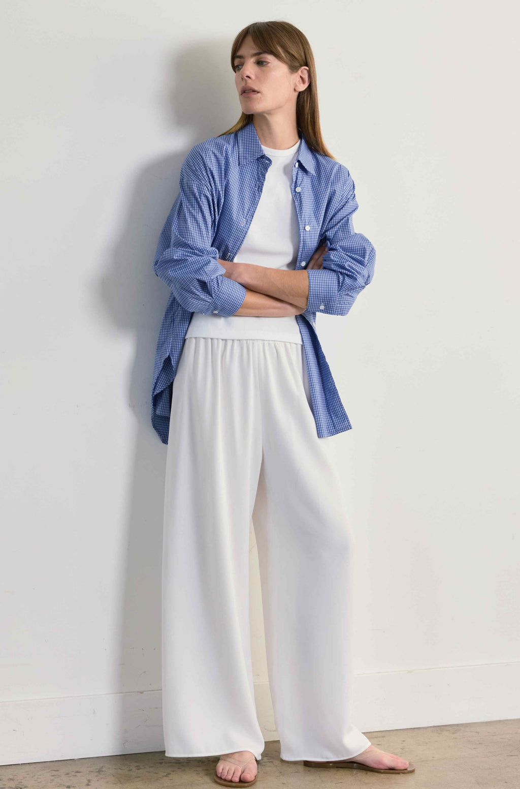 Woman wearing a blue shirt and white pants against a plain background