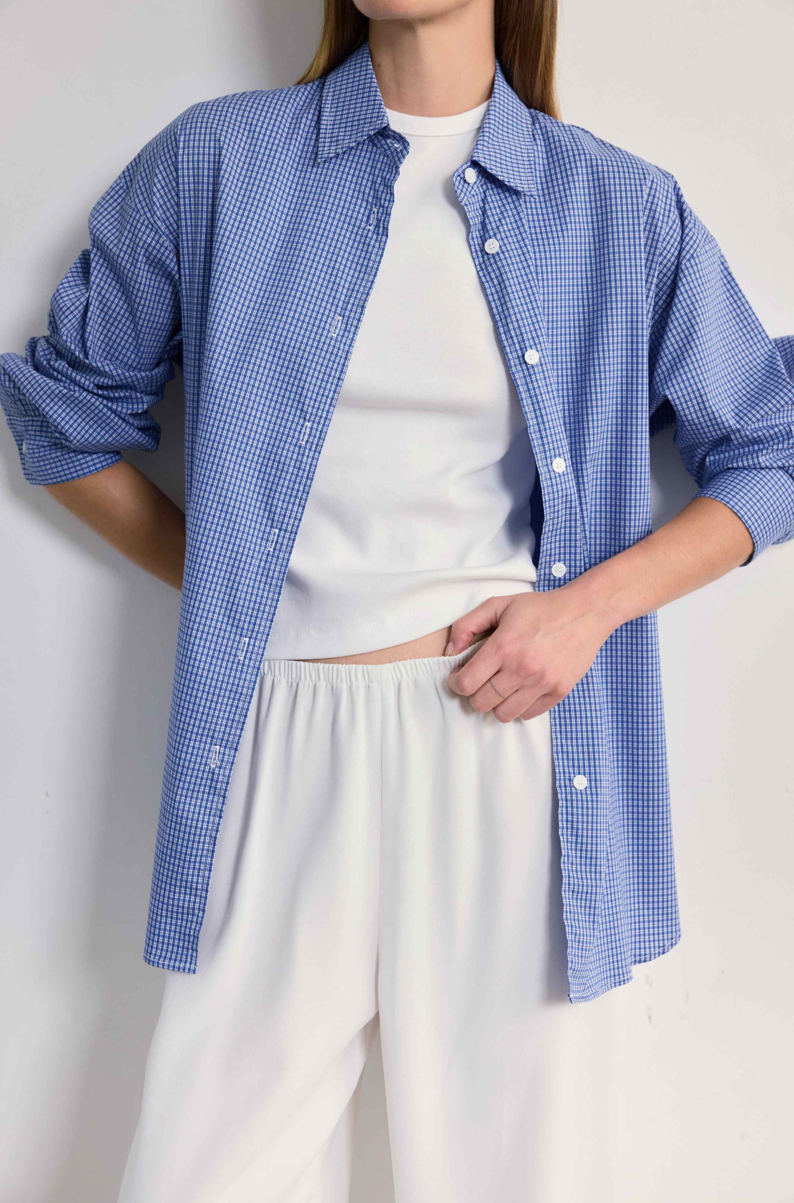 Person wearing a blue checkered shirt over a white top and pants on a light gray background