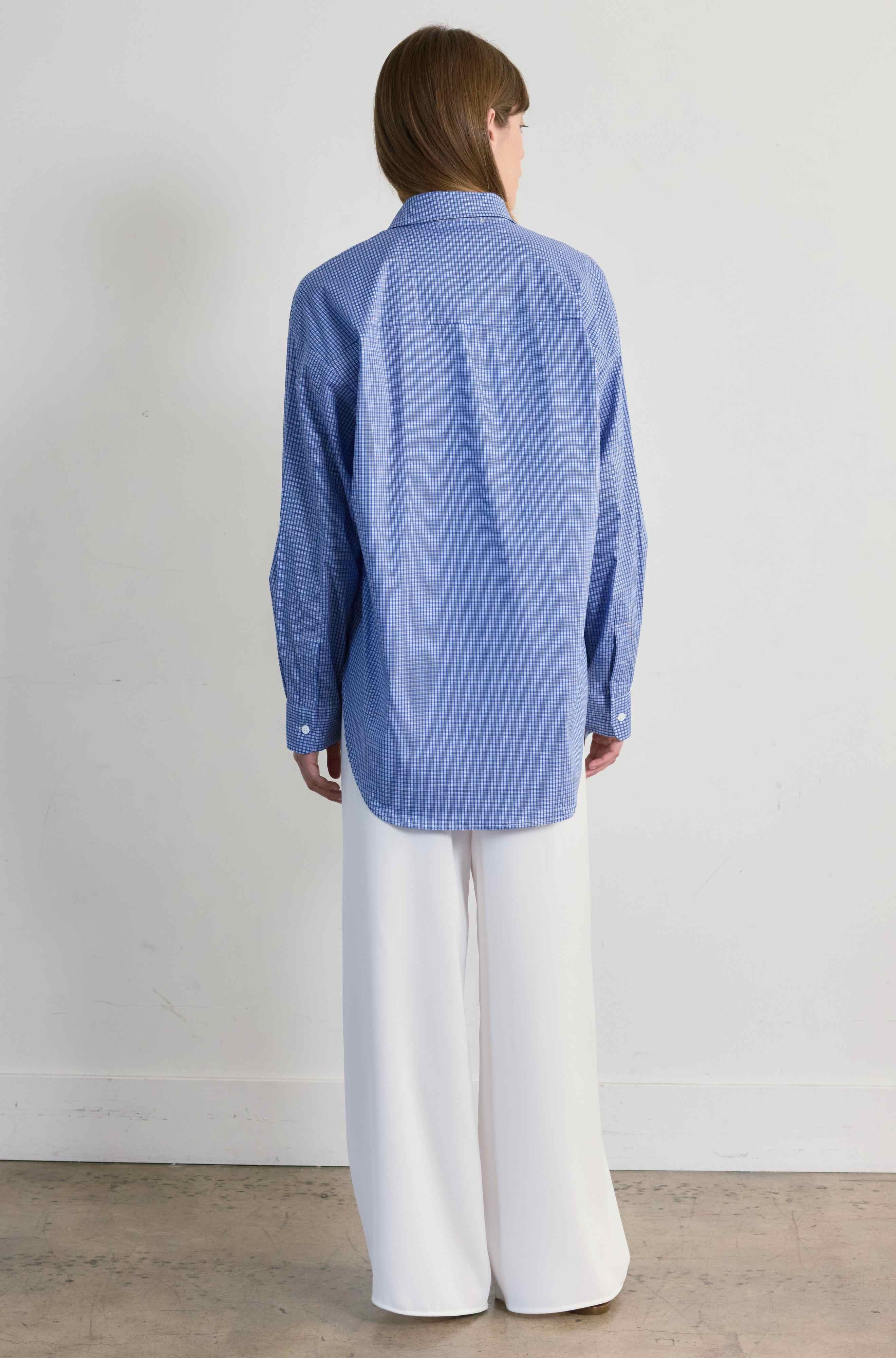 Person wearing a blue checkered shirt and white pants against a plain background