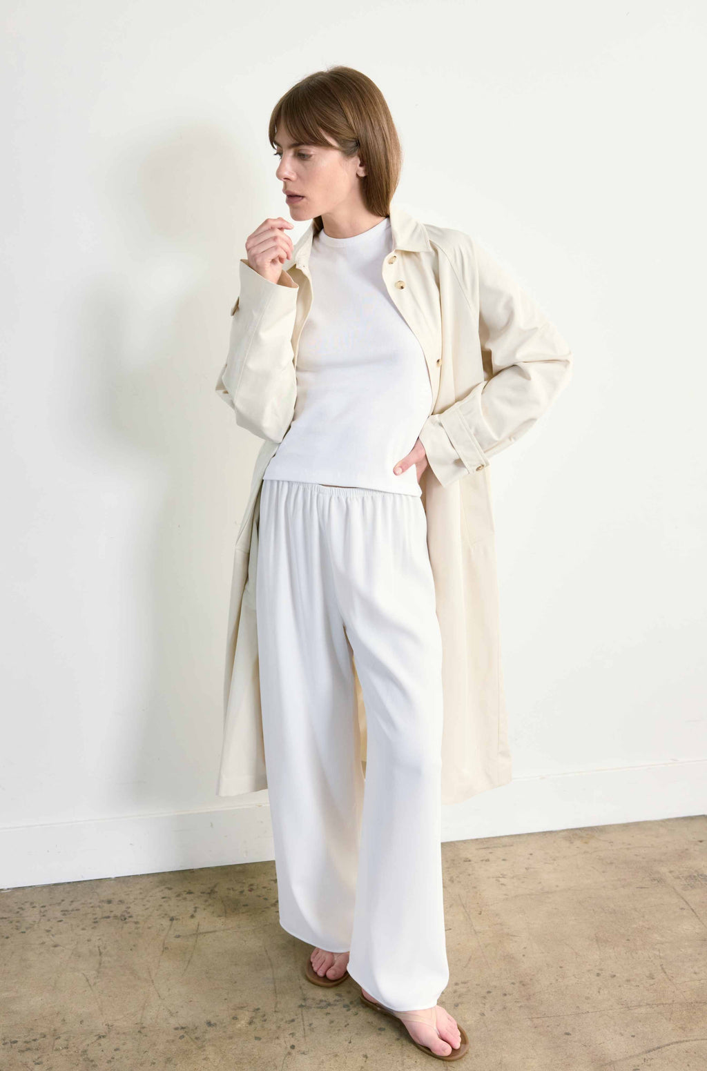 Woman wearing a white outfit under a beige button up trench coat