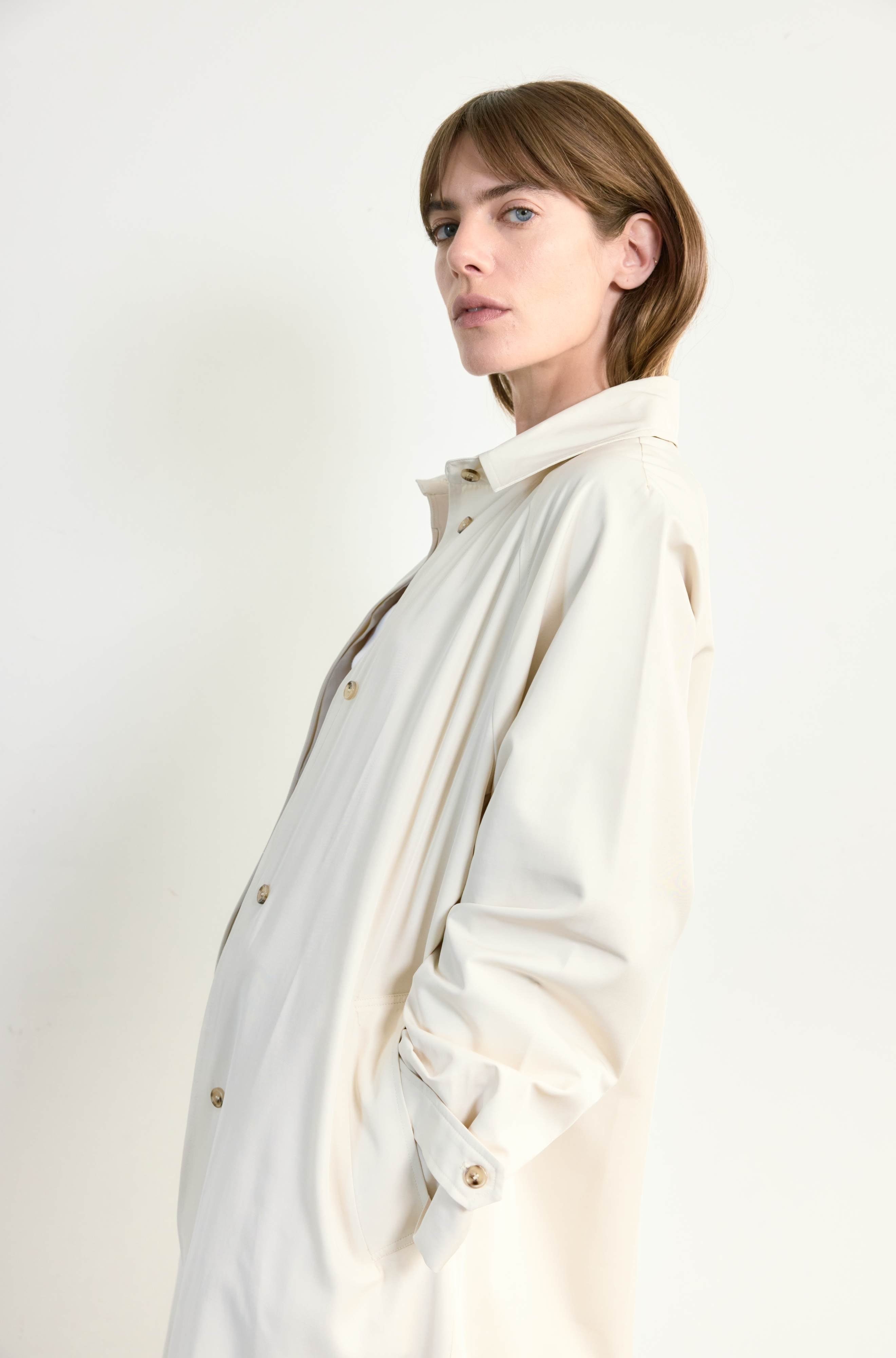 Woman wearing a beige coat with light brown buttons against a plain background