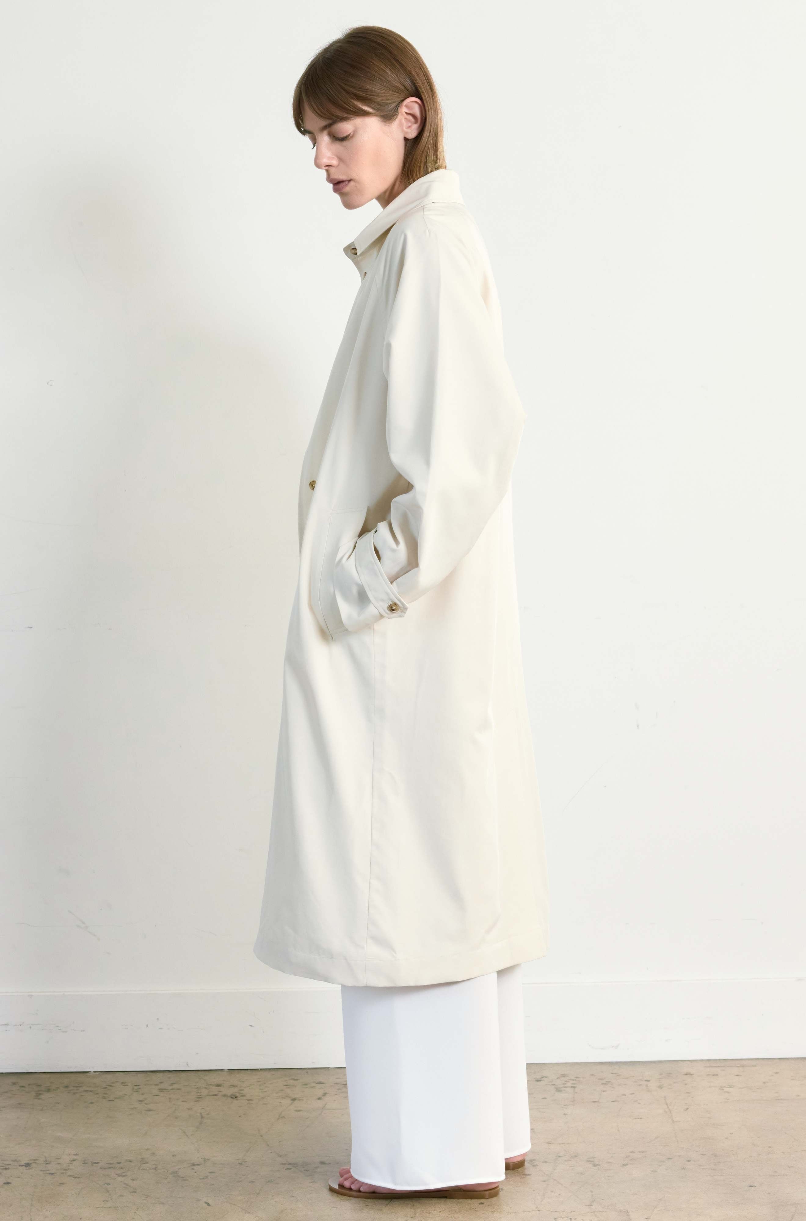 Person wearing a long cream coat against a white background