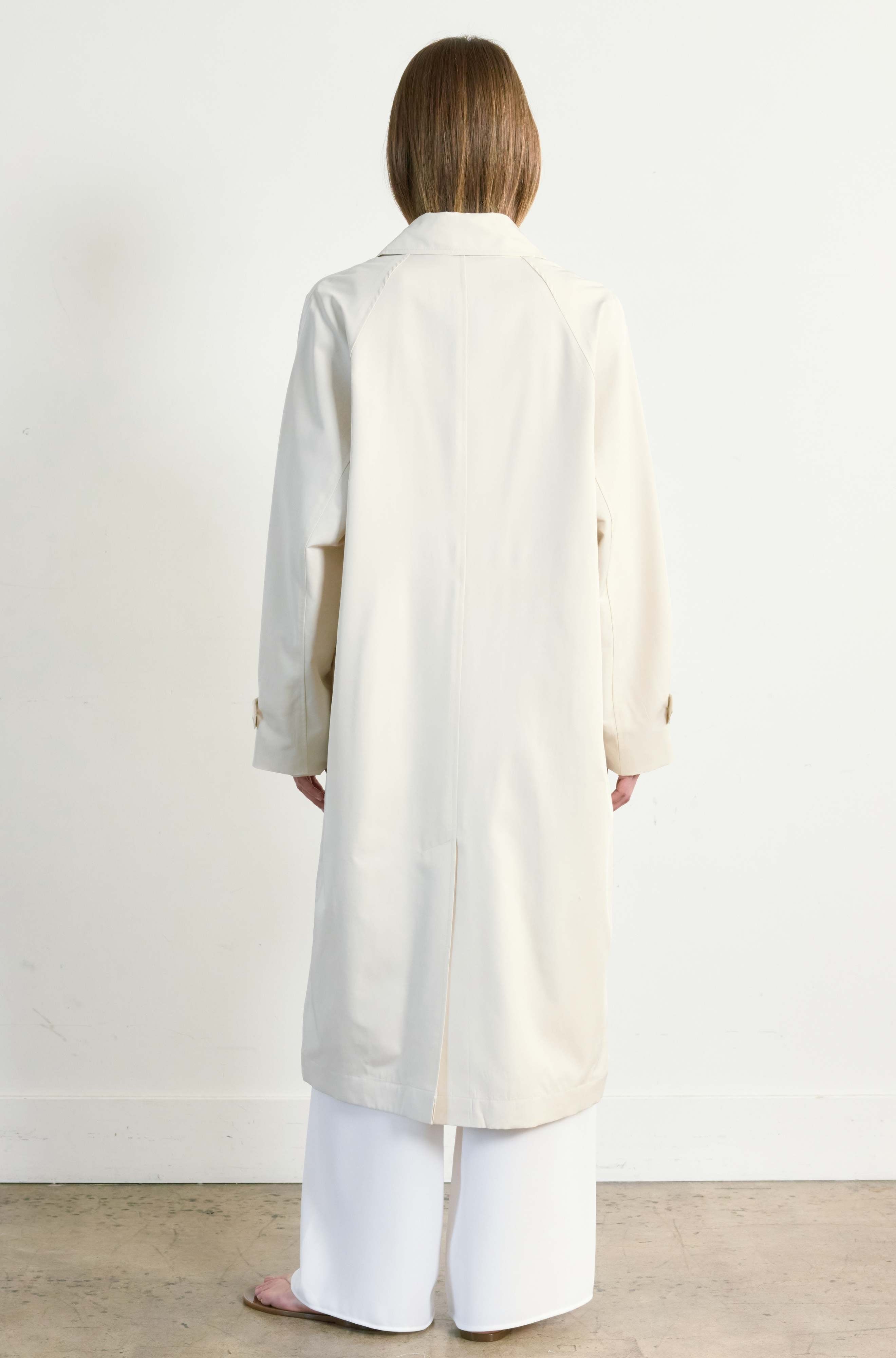 Person wearing a long cream coat standing against a white background