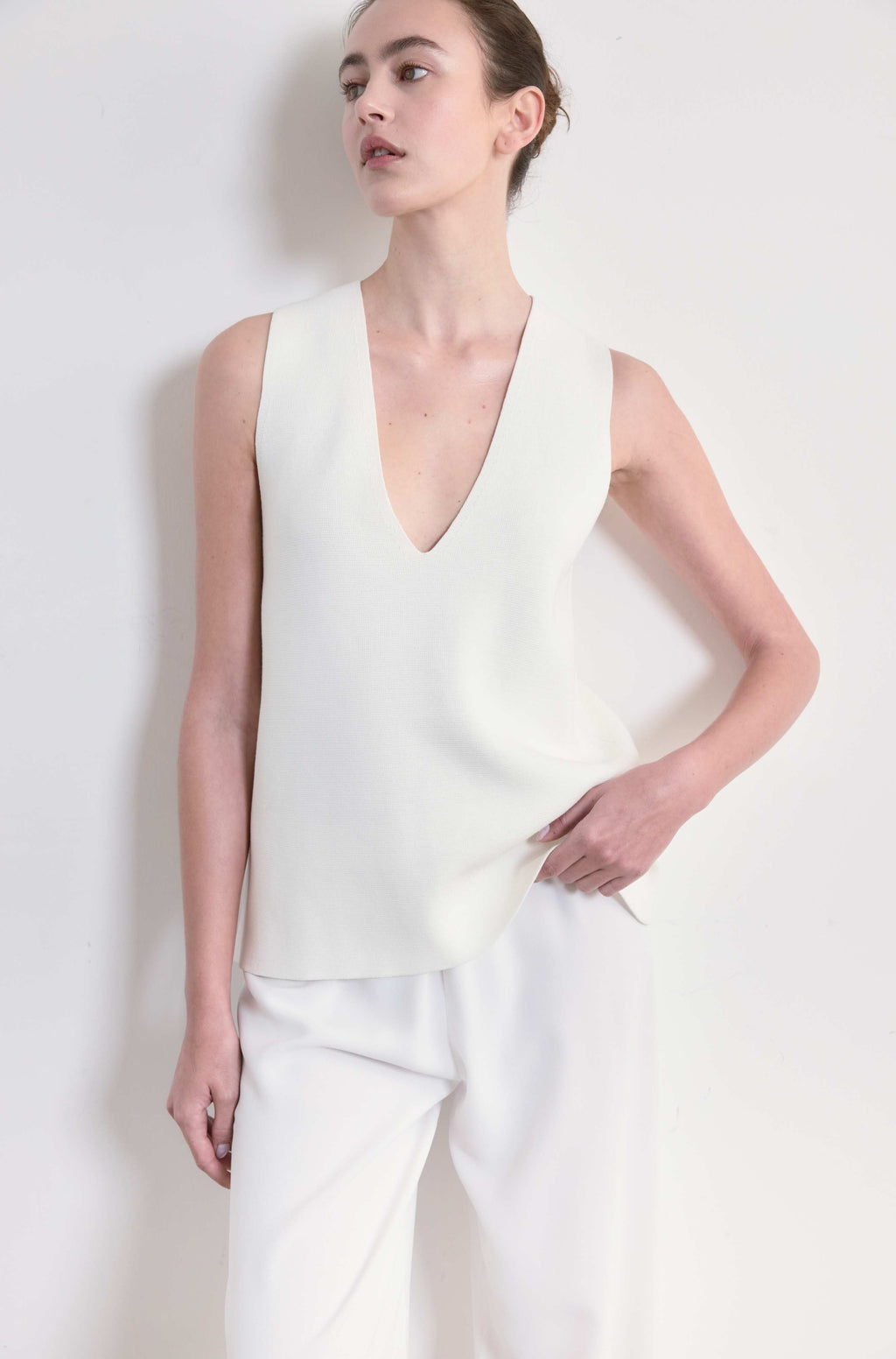 Woman wearing a white sleeveless top and pants against a plain background
