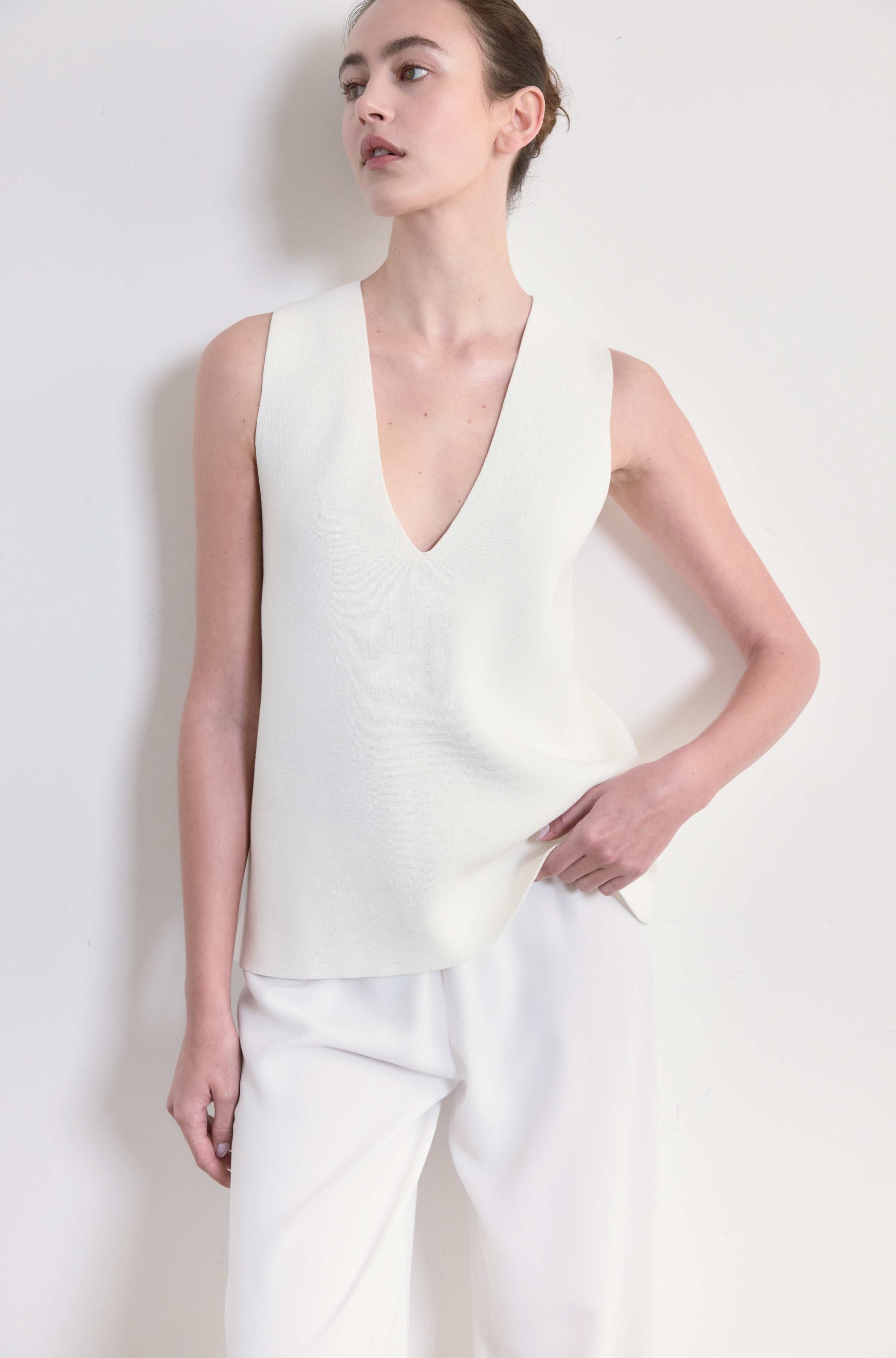 Woman wearing a white sleeveless top and pants against a plain background
