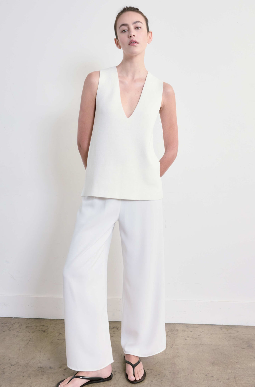 Person wearing a white sleeveless top and white pants against a plain background