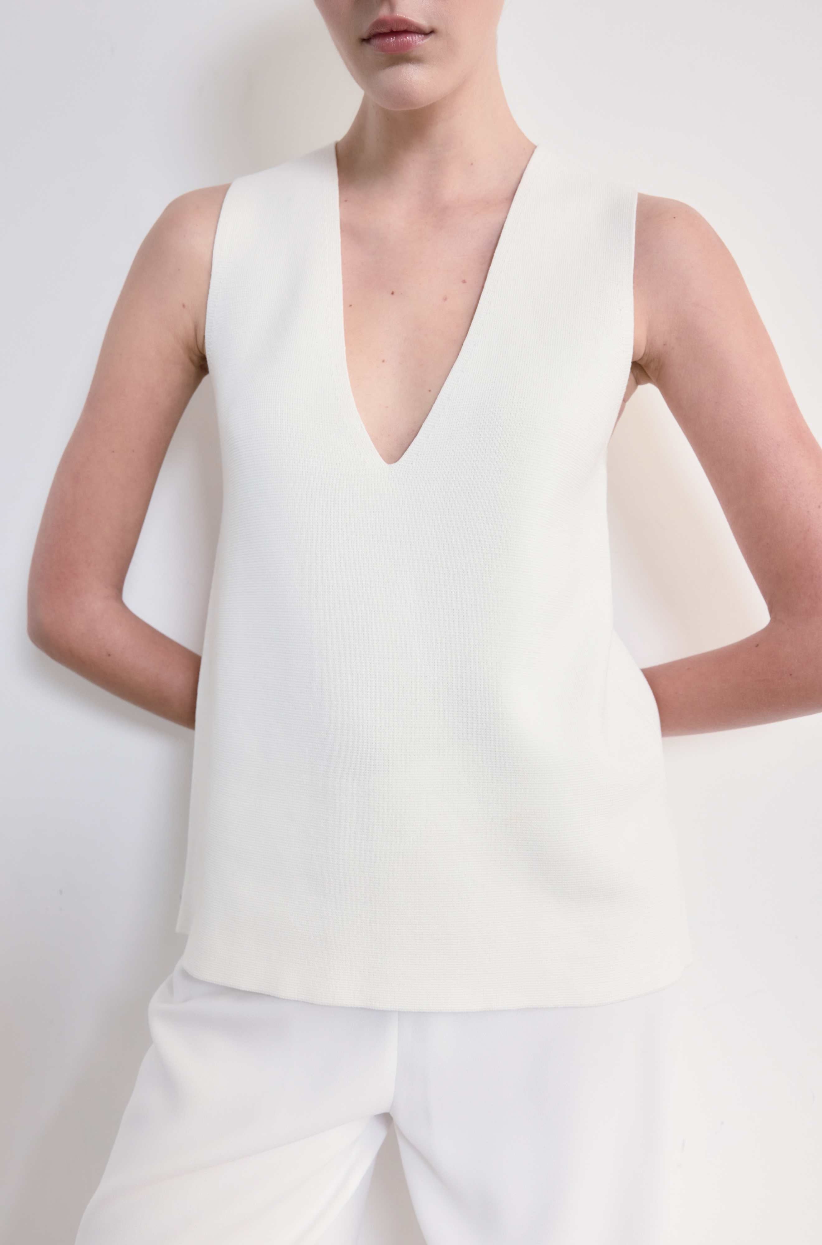 Person wearing a white sleeveless top against a plain background