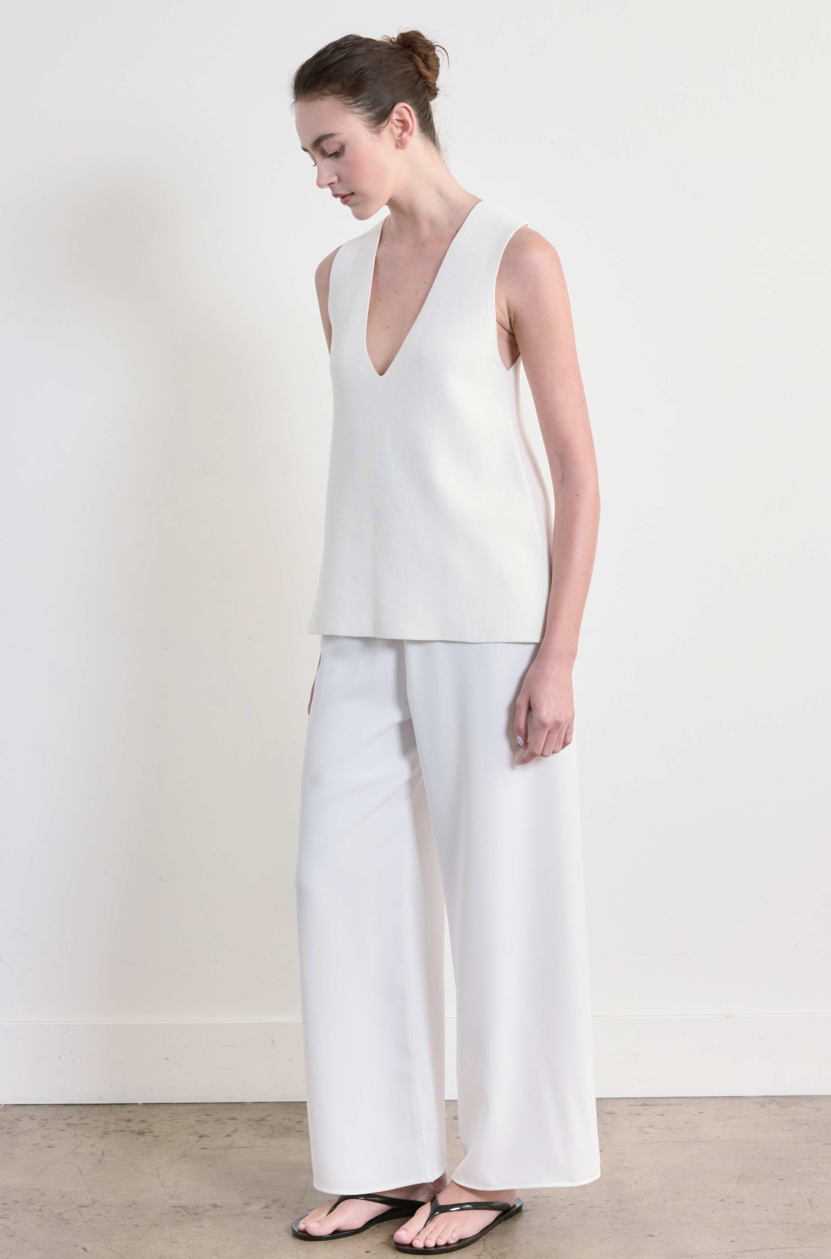 Woman wearing a white sleeveless top and wide-leg pants against a plain background