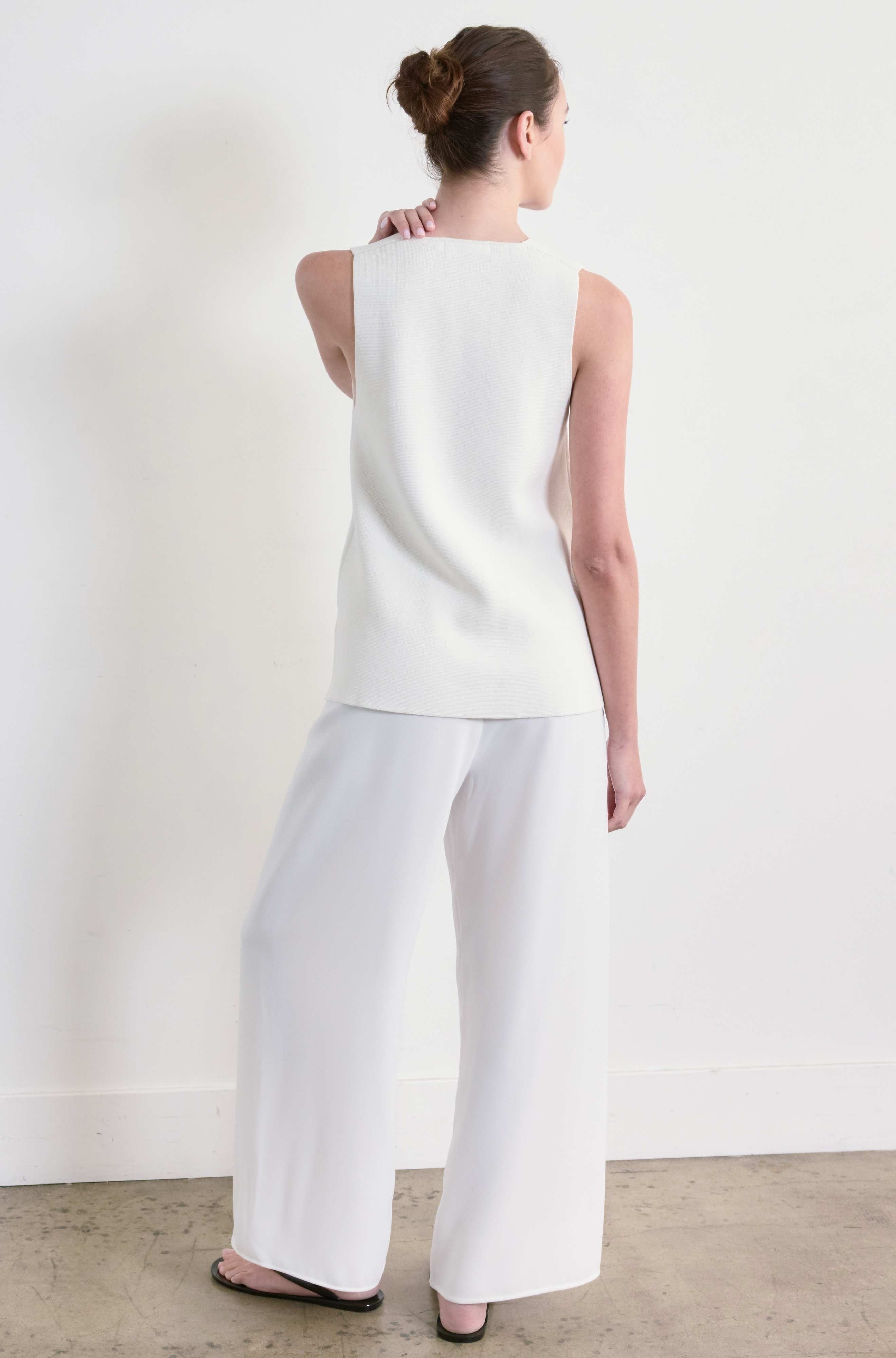 Woman wearing a white sleeveless top and white pants against a plain background